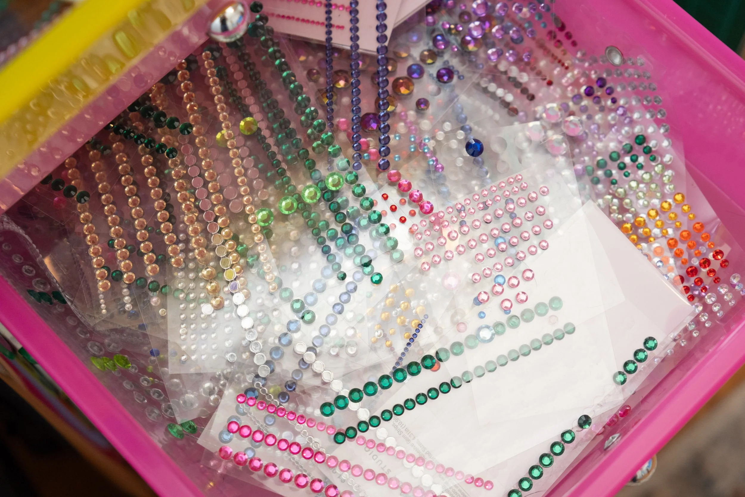 A pink box containing various colorful rhinestones and embellishments sorted by color and size.