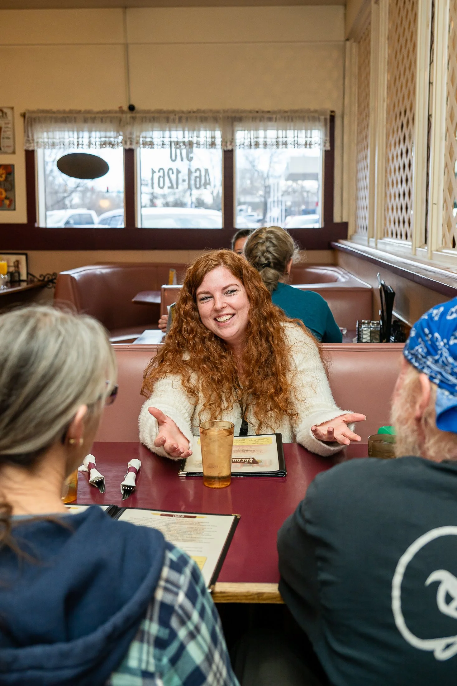 Female diner smiling at two people sitting across from her at a booth with a glass of water and two menus on the table.