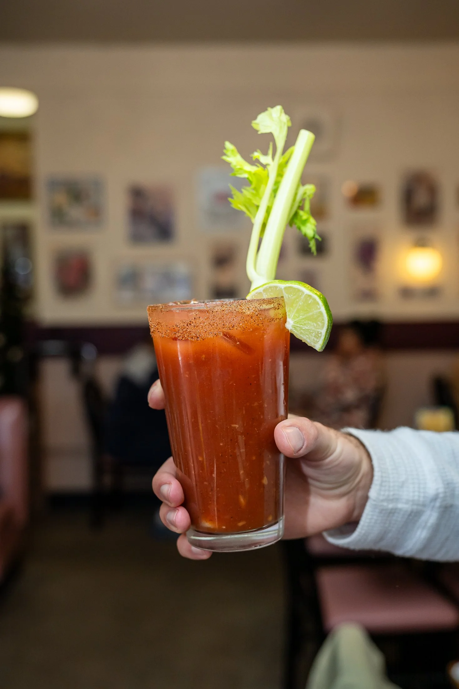 A hand holding a Bloody Mary brunch cocktail with celery and lime as a garnish.