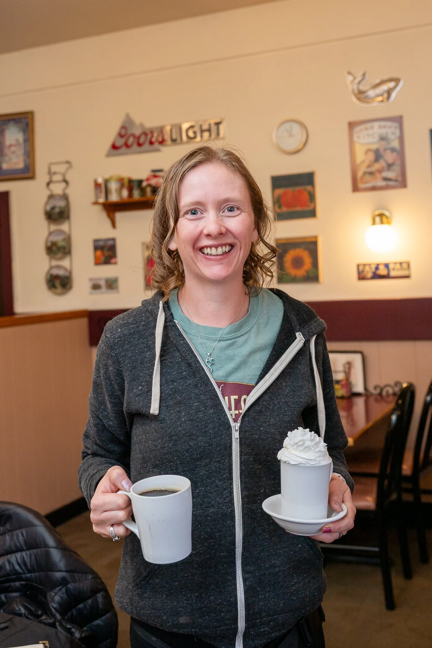 breakfast club server, Christine, holding one mug of hot cocoa and one mug of coffee