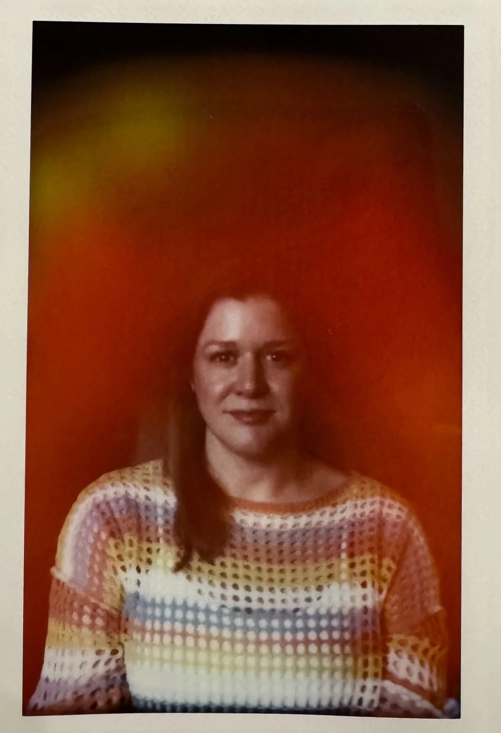 Portrait of a woman with shoulder-length brown hair wearing a colorful, patterned knit sweater, standing against a red background.