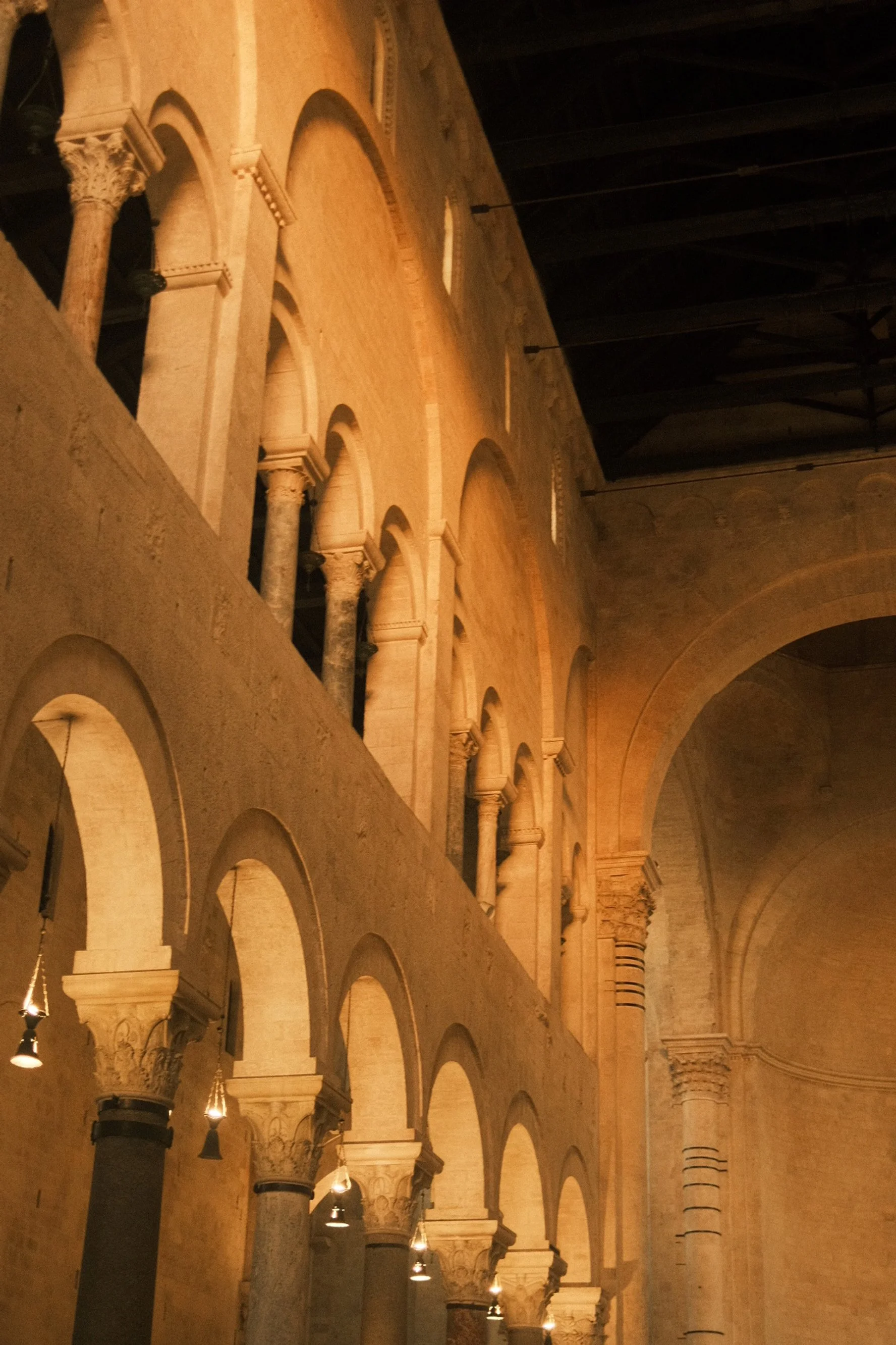 Interior view of a historic church or cathedral with tall arches, columns, and high vaulted ceilings, illuminated by warm lighting.