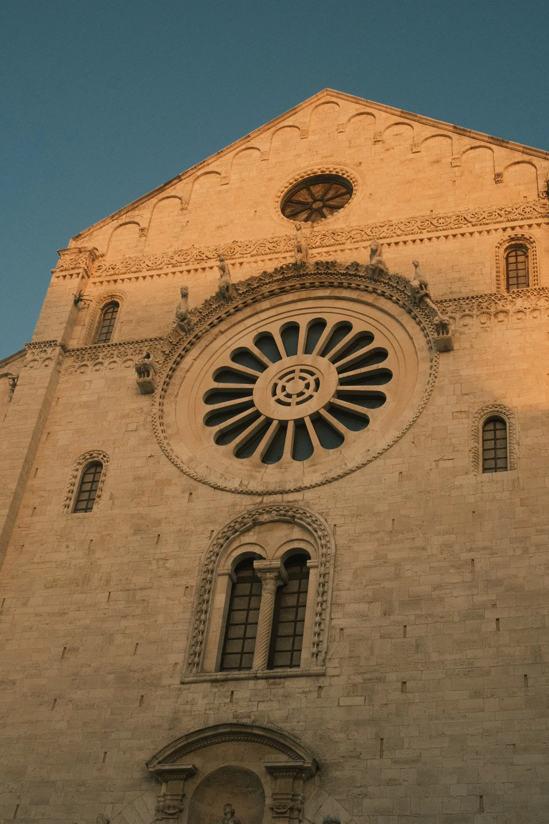 Close-up of a historic church facade with a large circular rose window and smaller arched windows, bathed in warm sunset light.