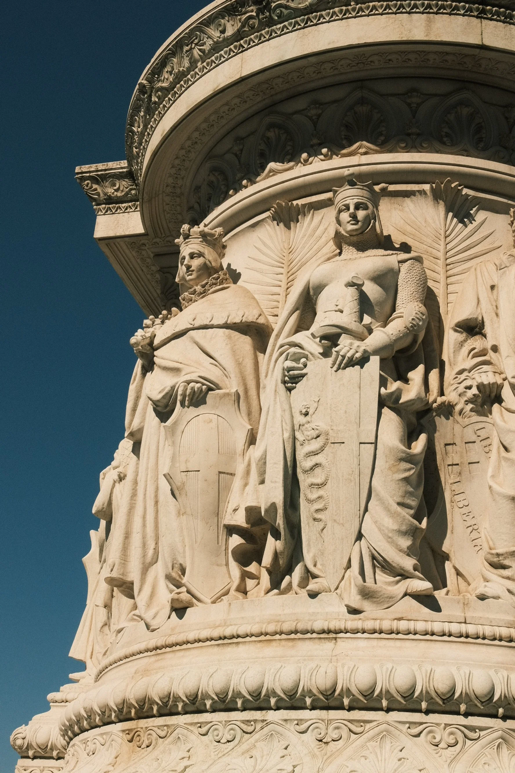 Close-up of the detailed marble sculpture on the Lincoln Memorial monument, featuring two seated allegorical figures representing justice and law, with a deep blue sky in the background.