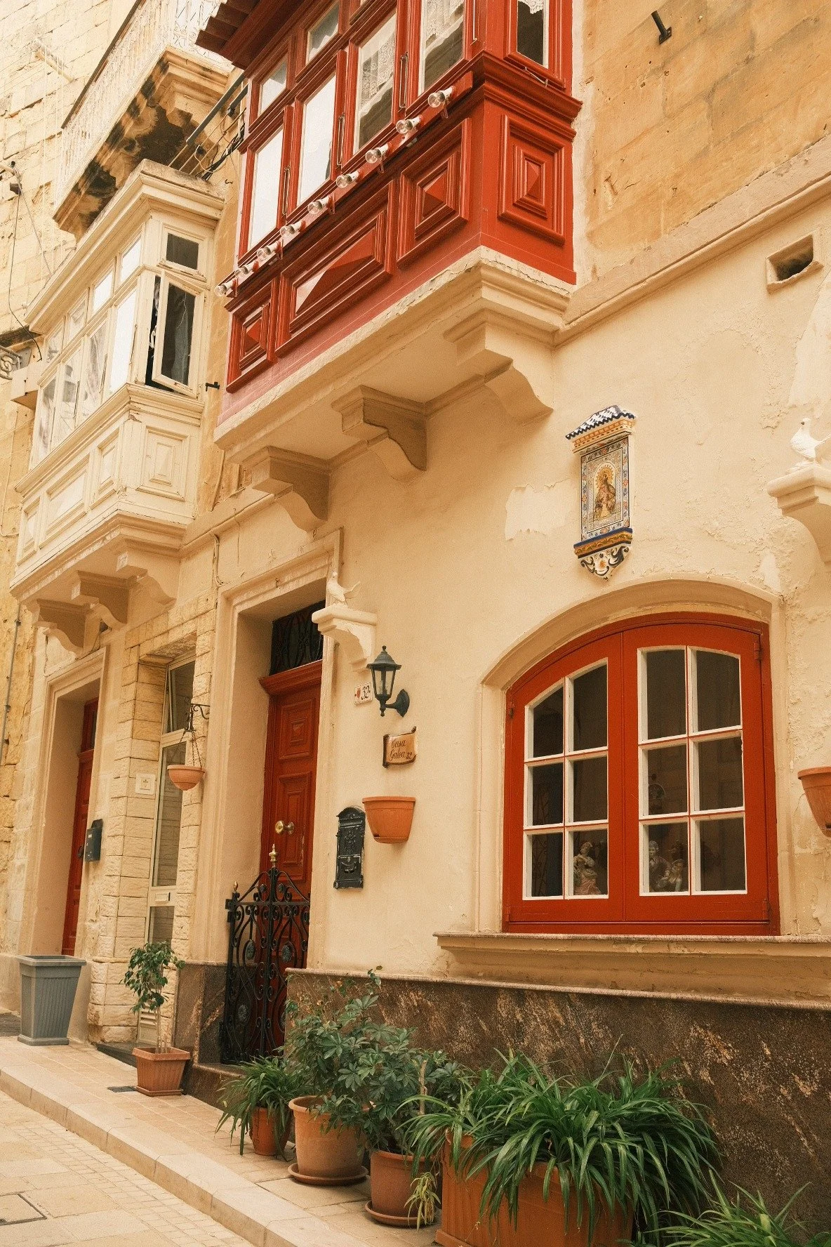 Exterior of a charming European-style house with potted plants, arched windows, and decorated balconies.