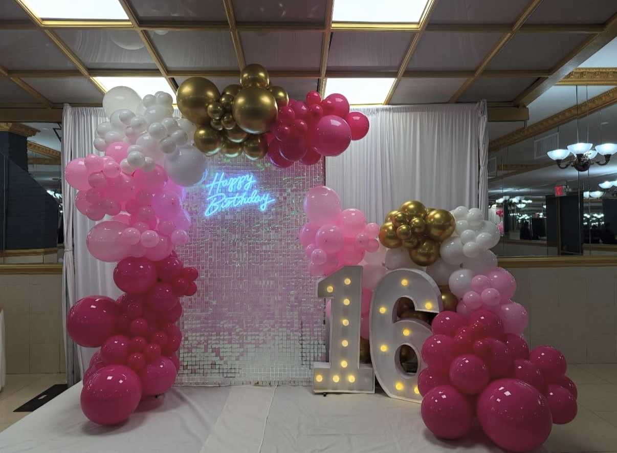 Decorative birthday backdrop with pink, white, and gold balloons, a neon sign reading 'Happy Birthday,' and a large illuminated '16' for a 16th birthday celebration.