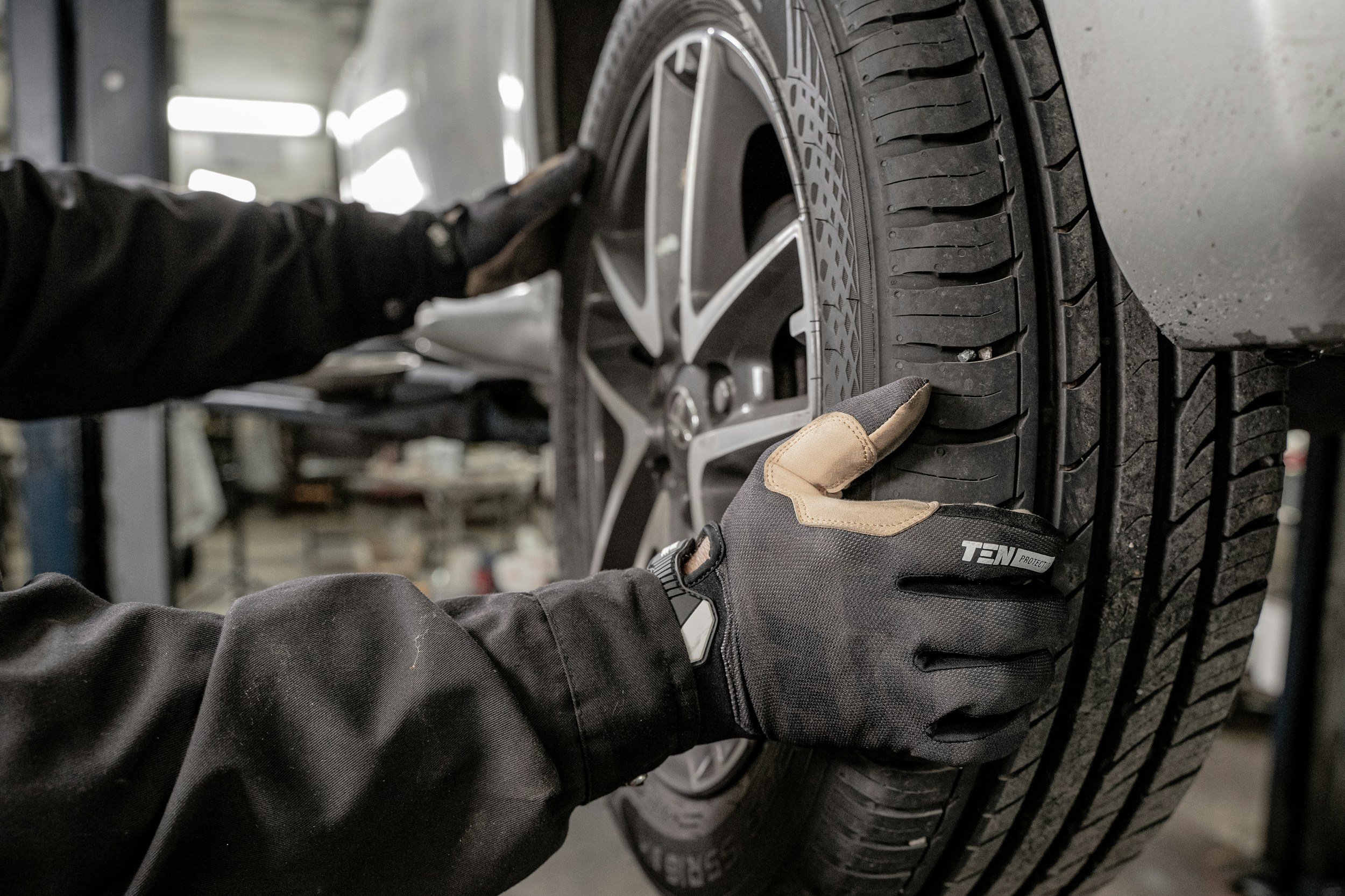 A mechanic installing or inspecting an automobile tire with a tire wrench in a workshop.