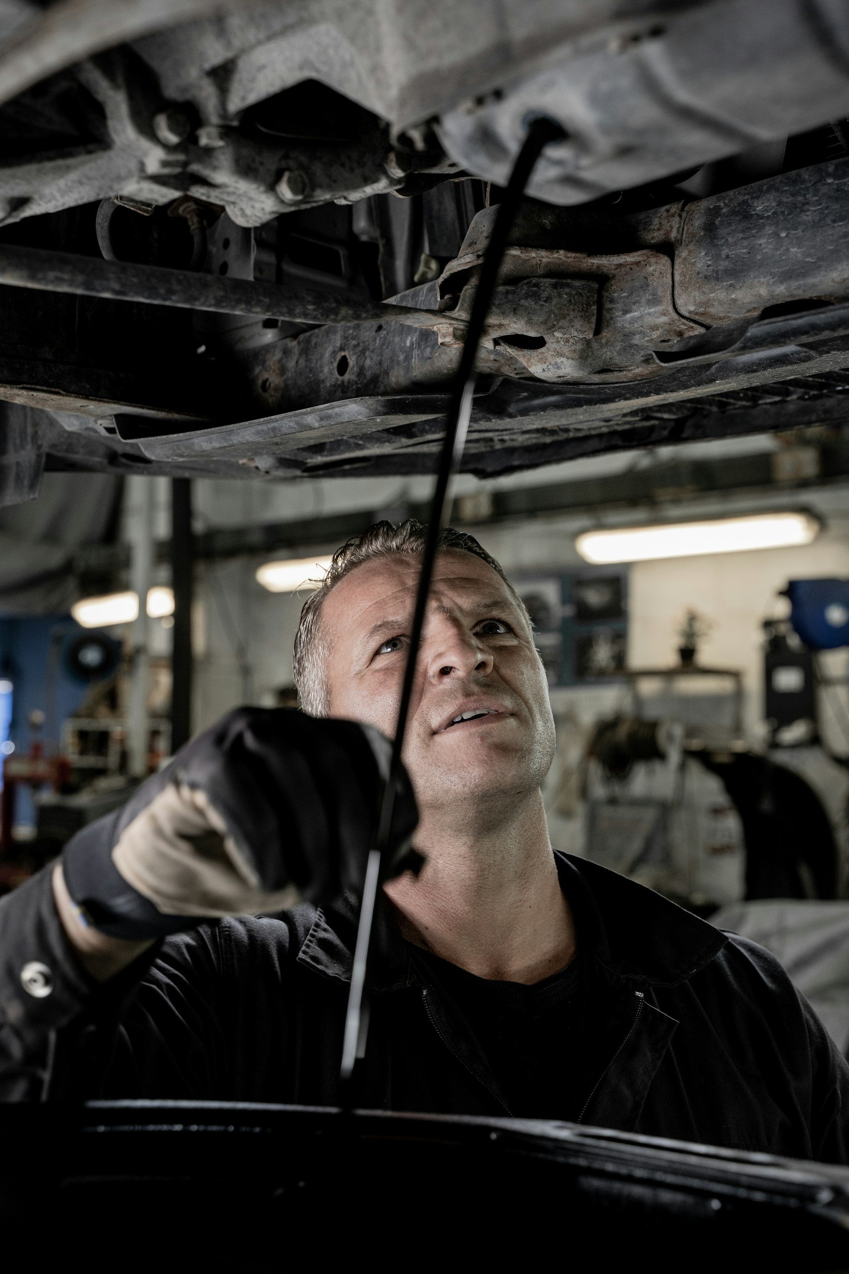 A mechanic inspecting a car's underside in a garage.