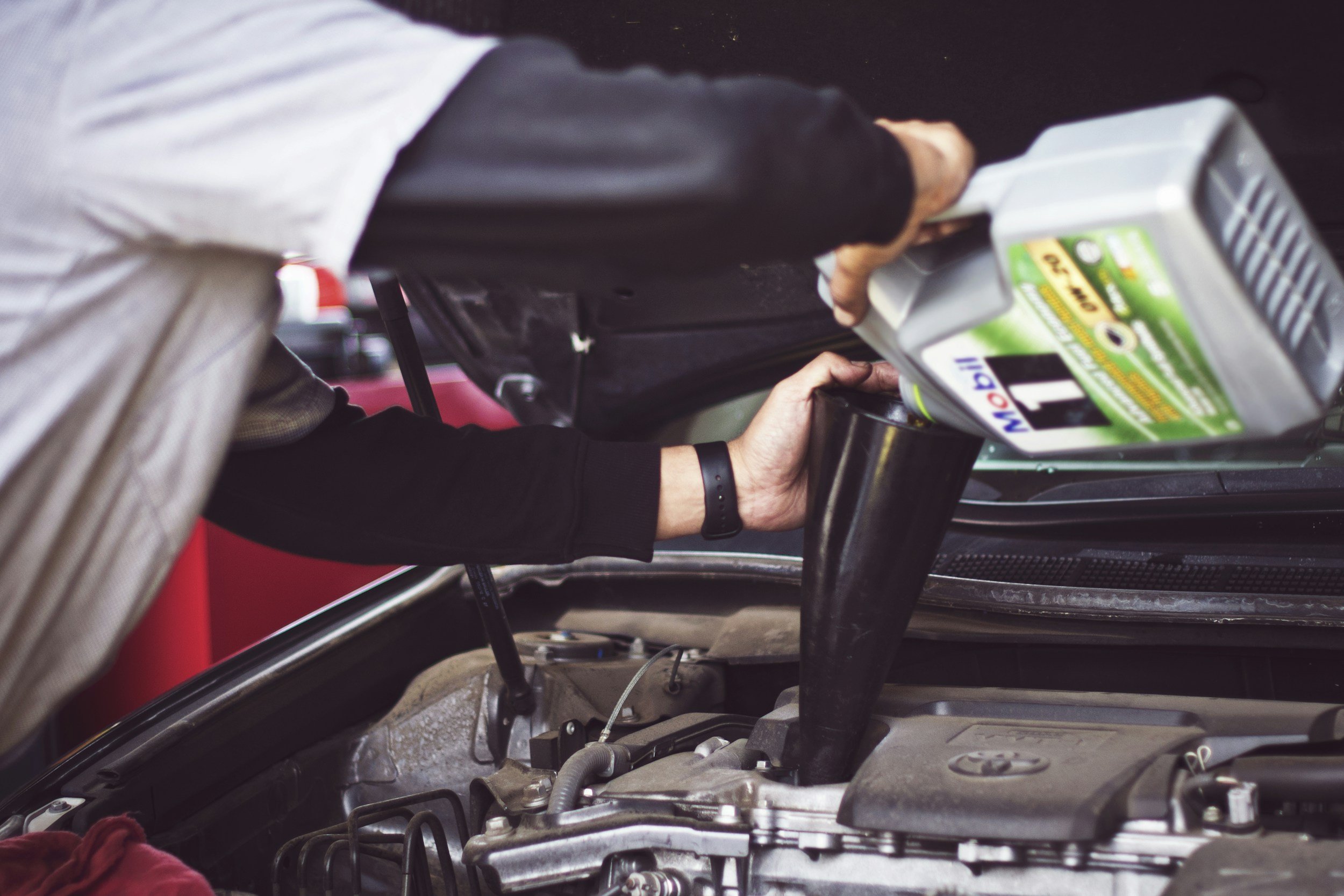 Person filling car with motor oil under the hood of a vehicle.