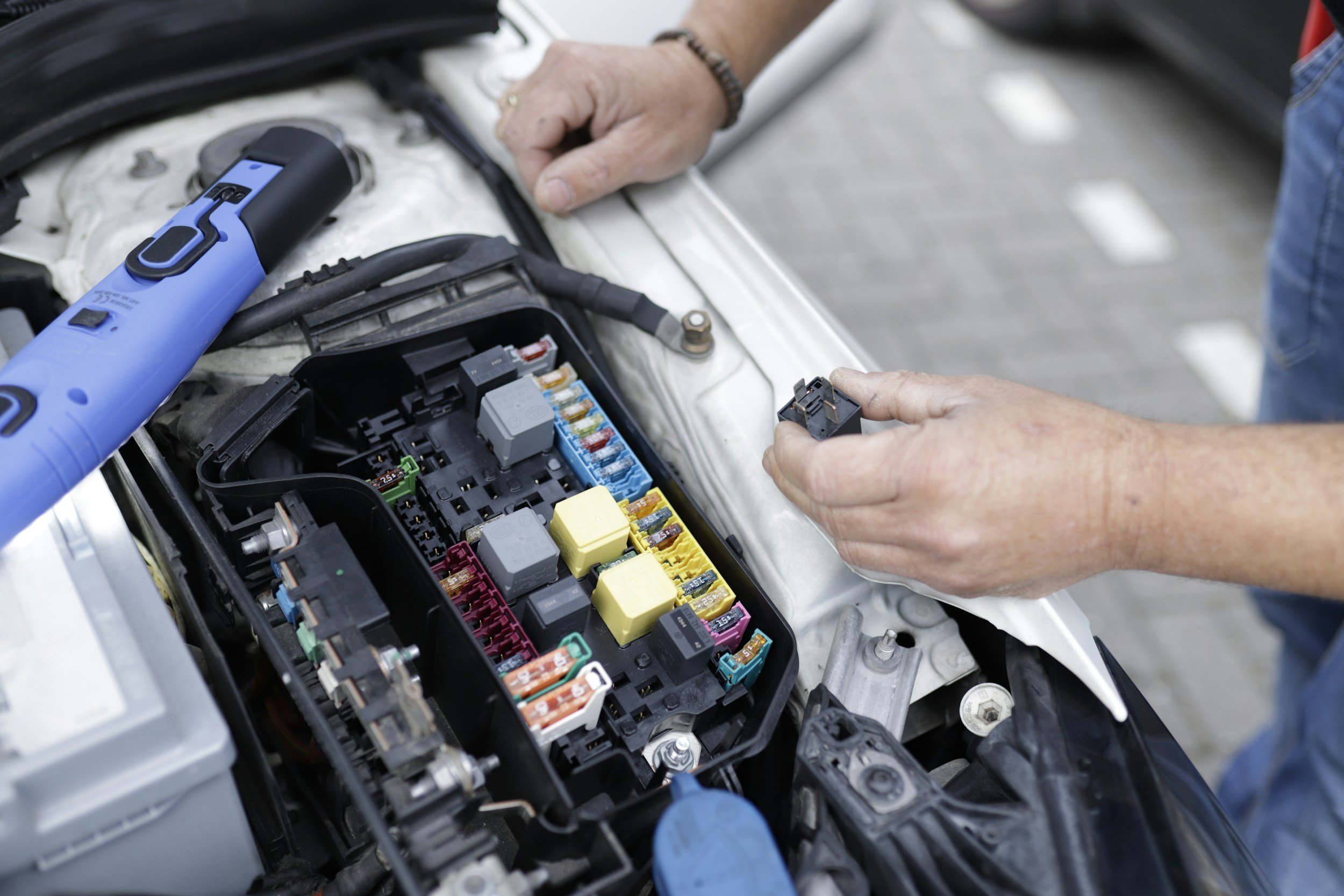 Person working on car's fuse box with diagnostic tool in hand.