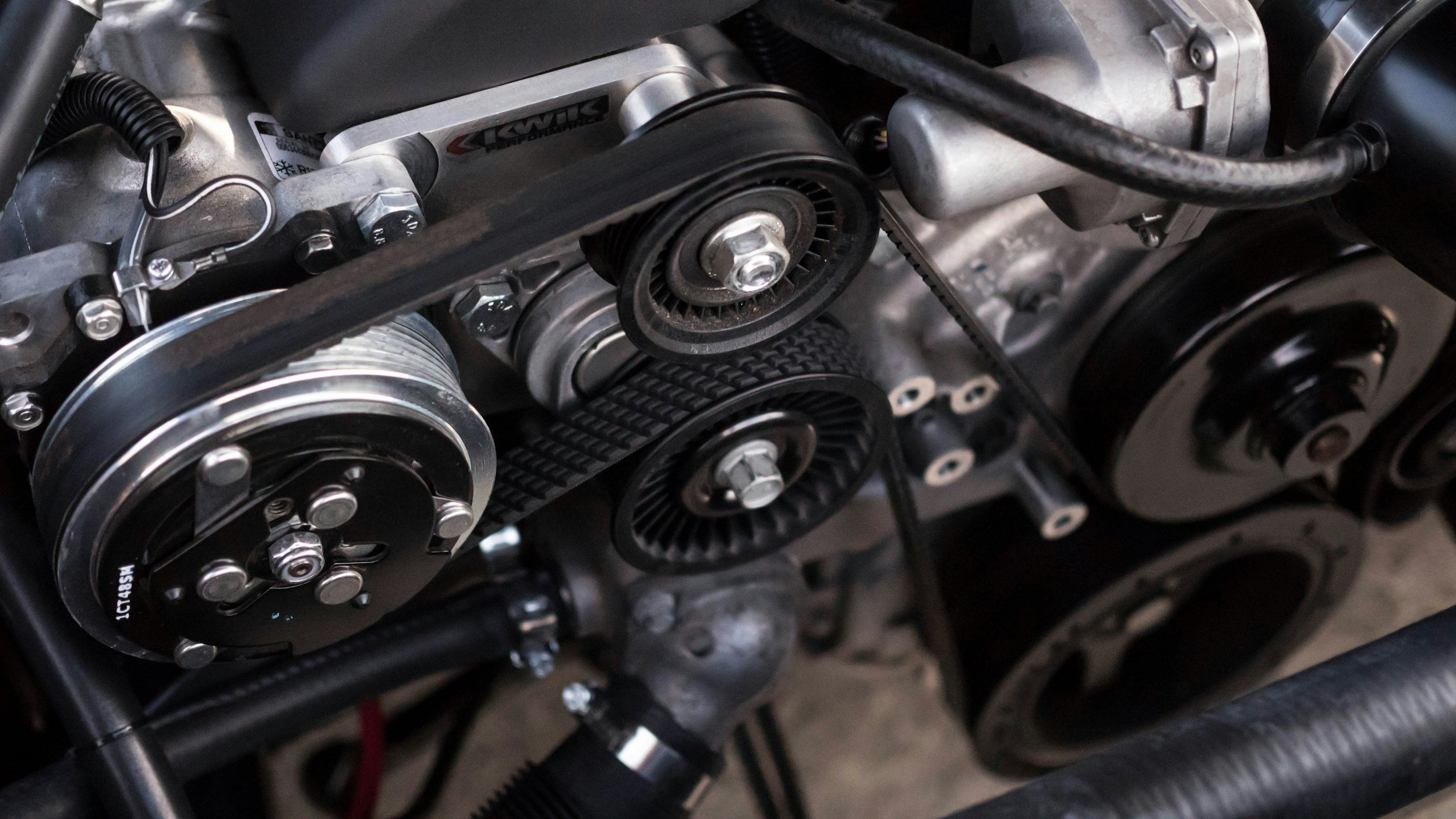 Close-up of a car engine showing belt, pulleys, and various metal parts.