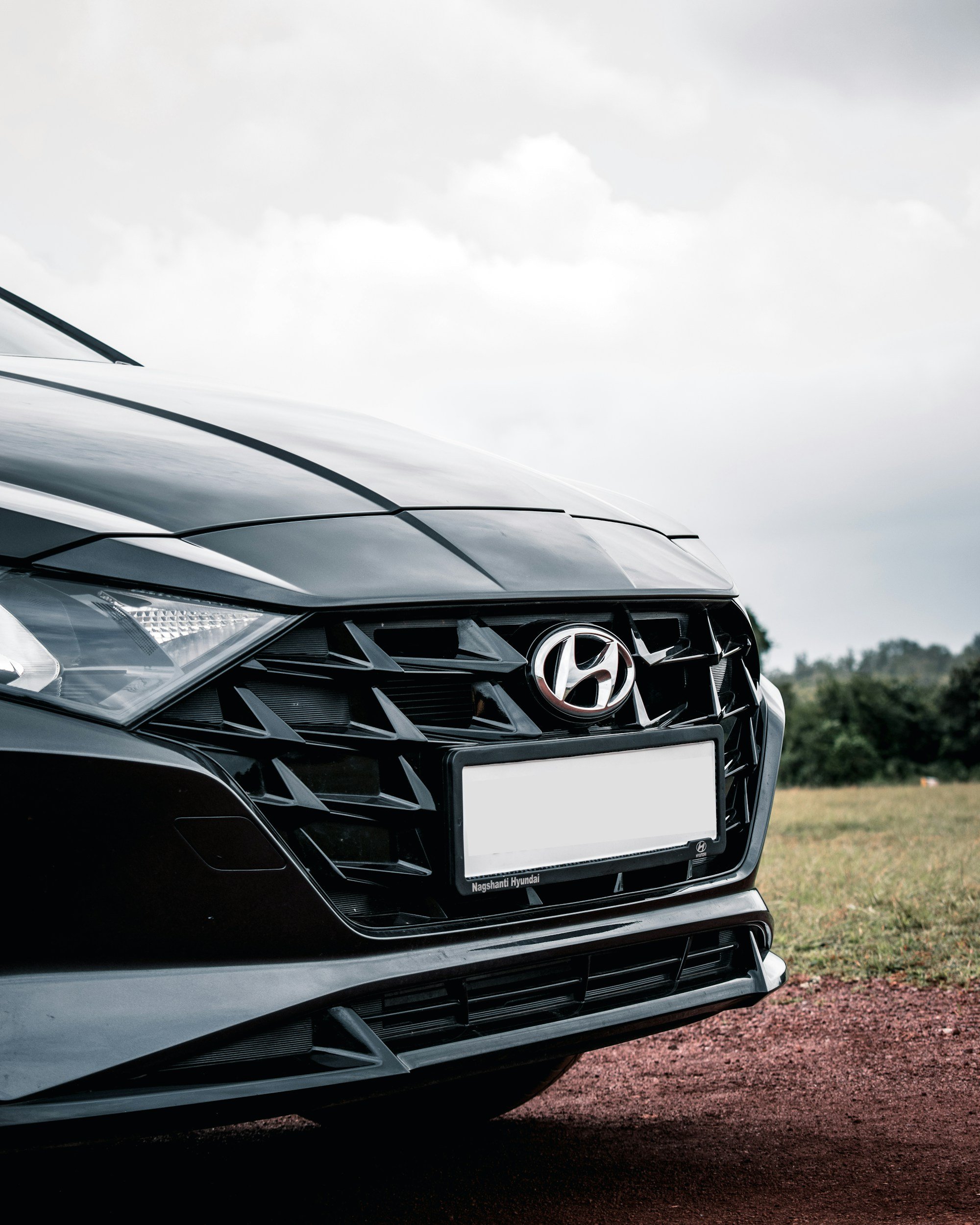 Front view of a black Hyundai car parked on grass with a cloudy sky in the background.