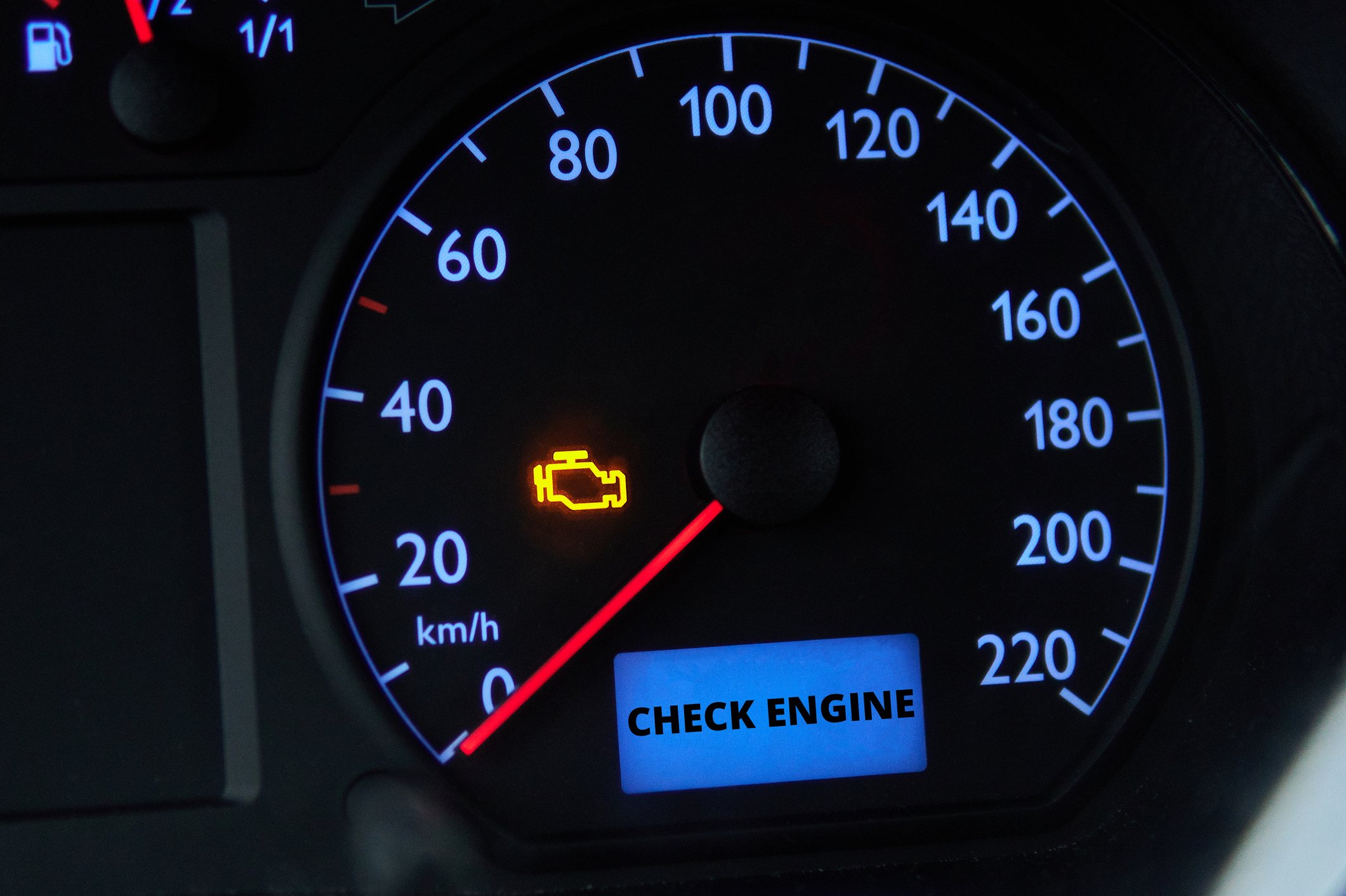 Car dashboard showing illuminated check engine light and message on digital display reading 'CHECK ENGINE'.