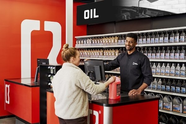 Customer and employee at a gas station counter, with shelves of motor oil containers behind them.