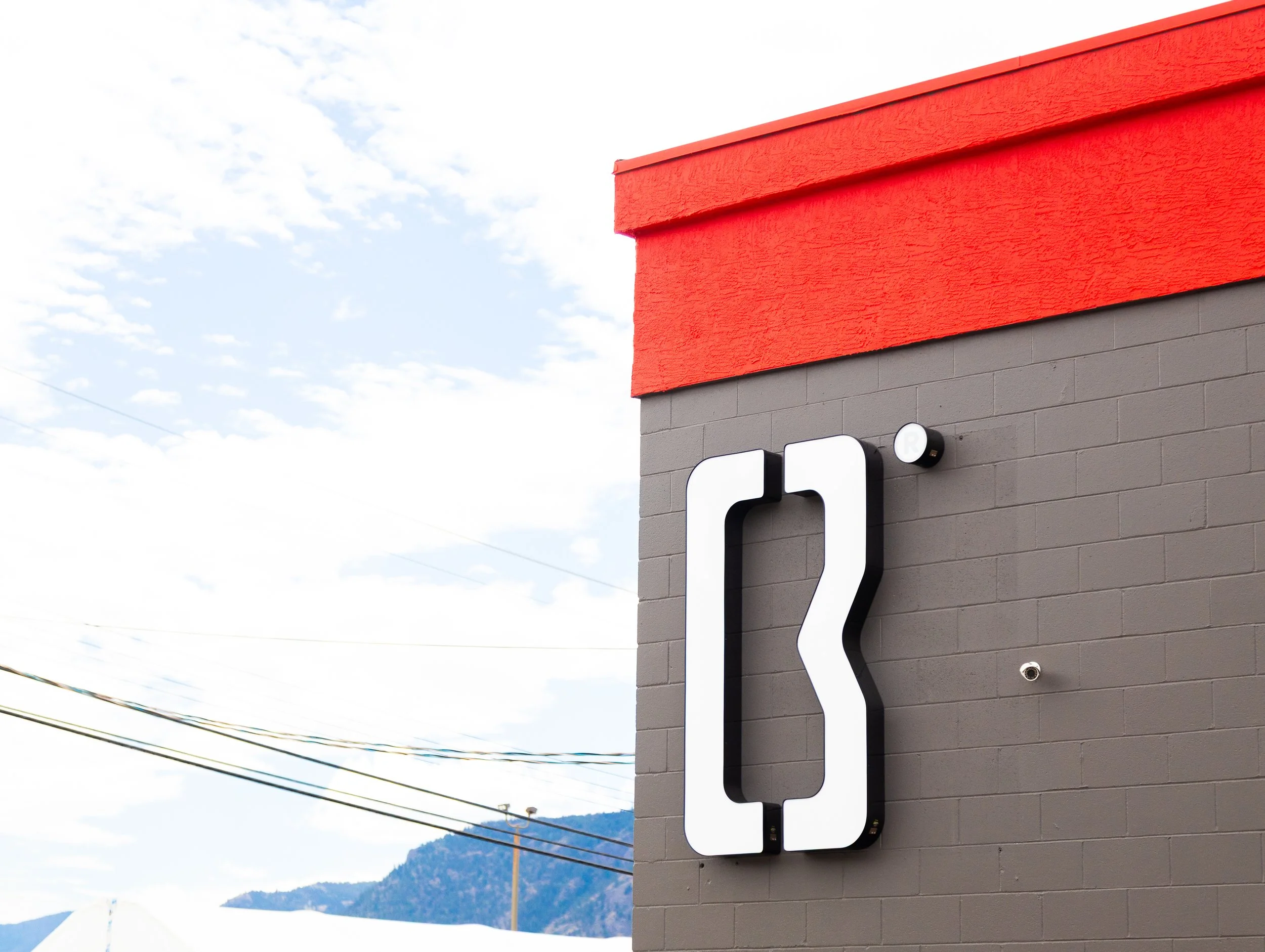 Modern building exterior with red and gray painted brick wall and large illuminated black and white canopy arrow sign.