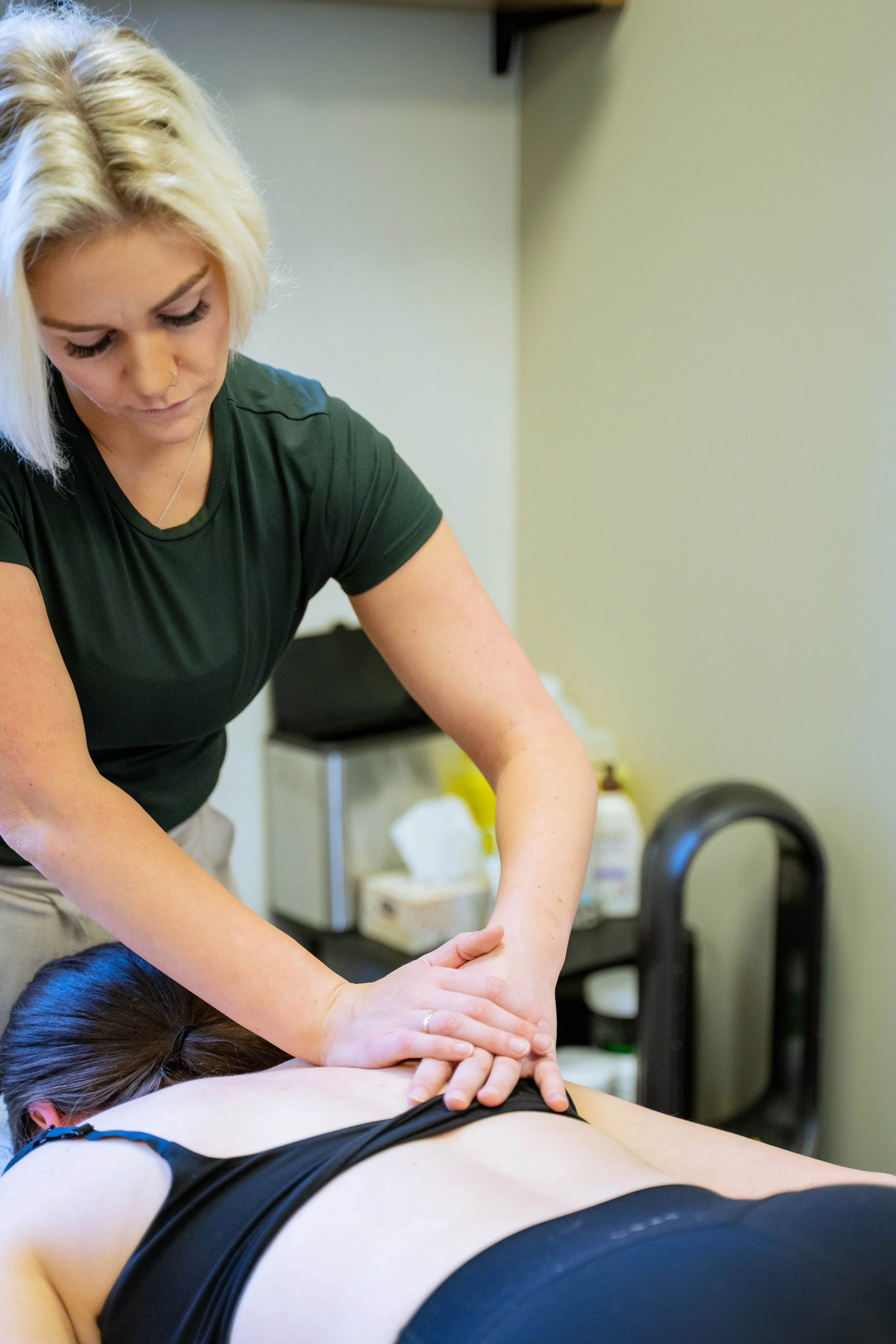 A woman giving a massage to another person lying face down on a massage table, with the therapist's hands on their back.