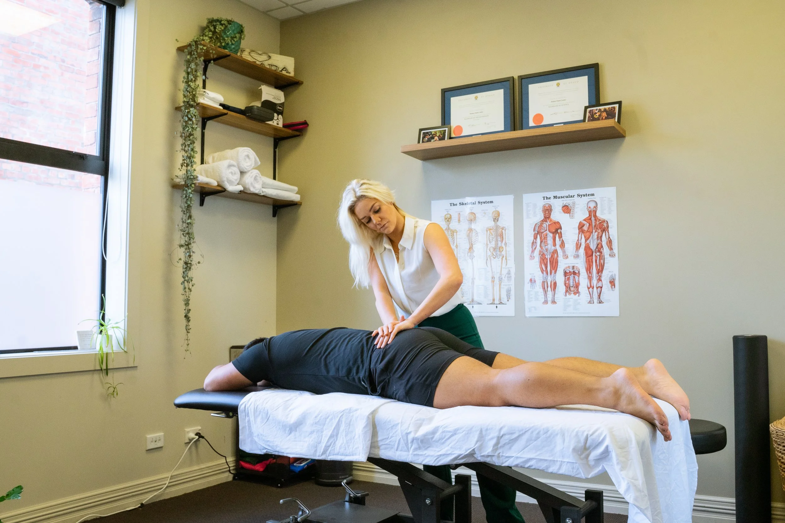 A woman receiving chiropractic treatment from a healthcare professional in an office with medical posters on the wall.