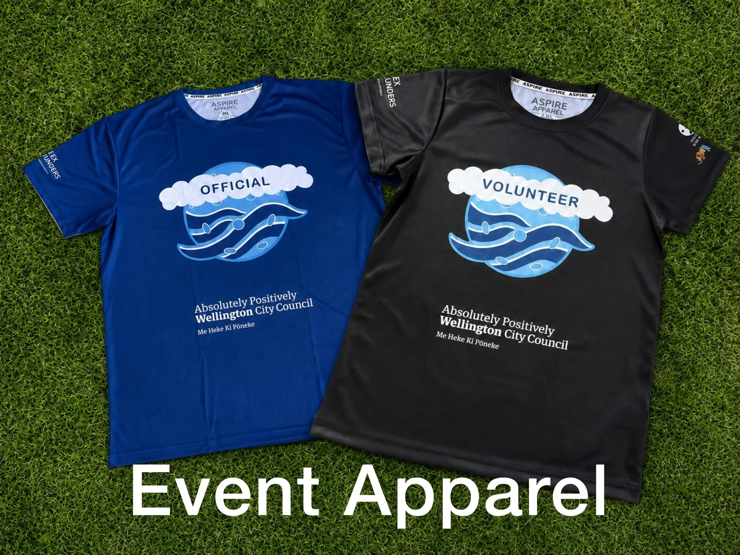 Blue official and black volunteer event T-shirts displayed on grass, featuring Wellington City Council branding and a wave logo
