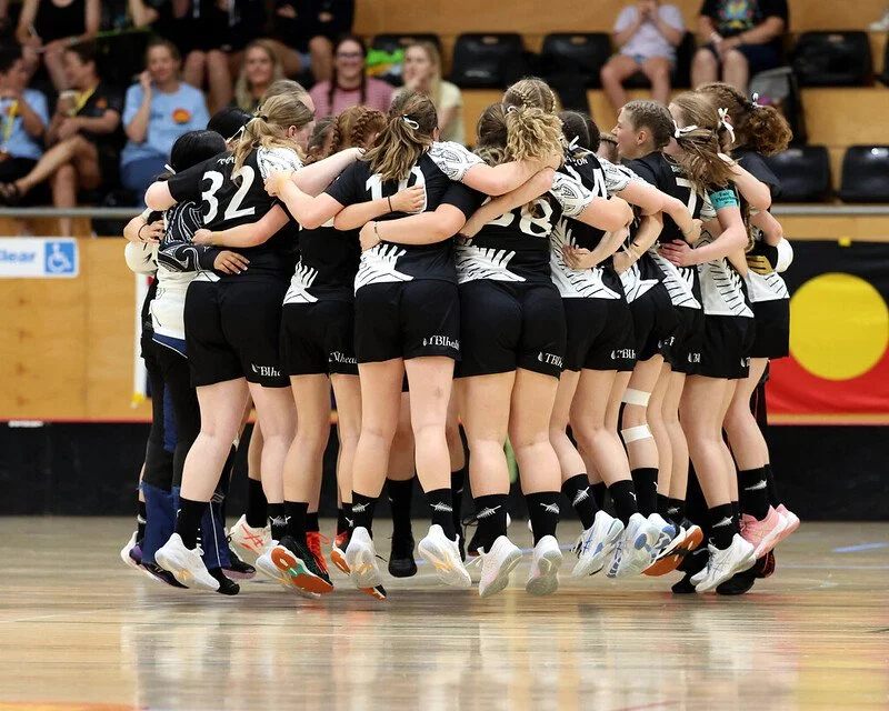 Women's indoor floorball team huddling and jumping together on a court during a game
