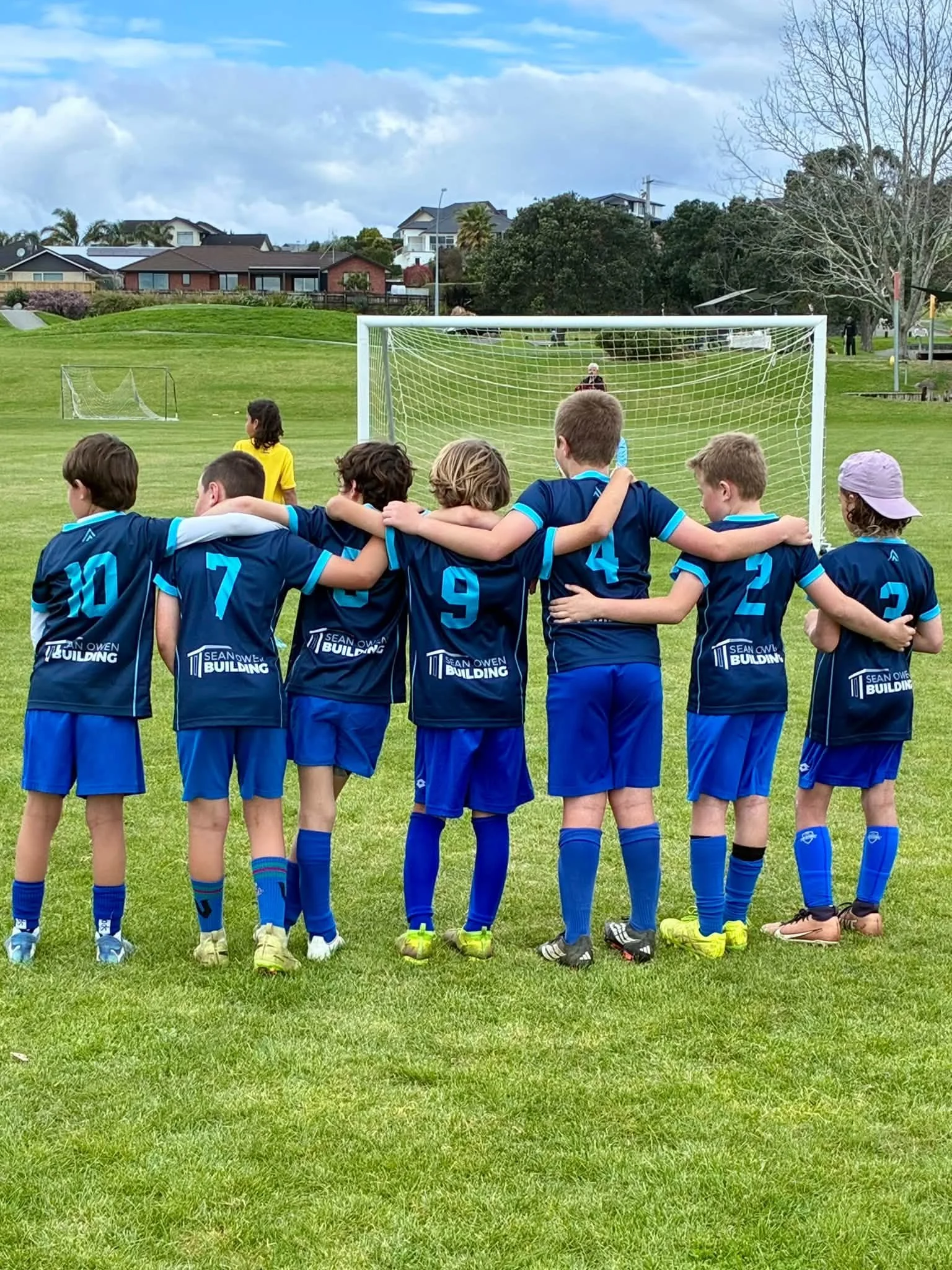 Youth soccer team in blue uniforms huddling in front of a goal on a grassy field