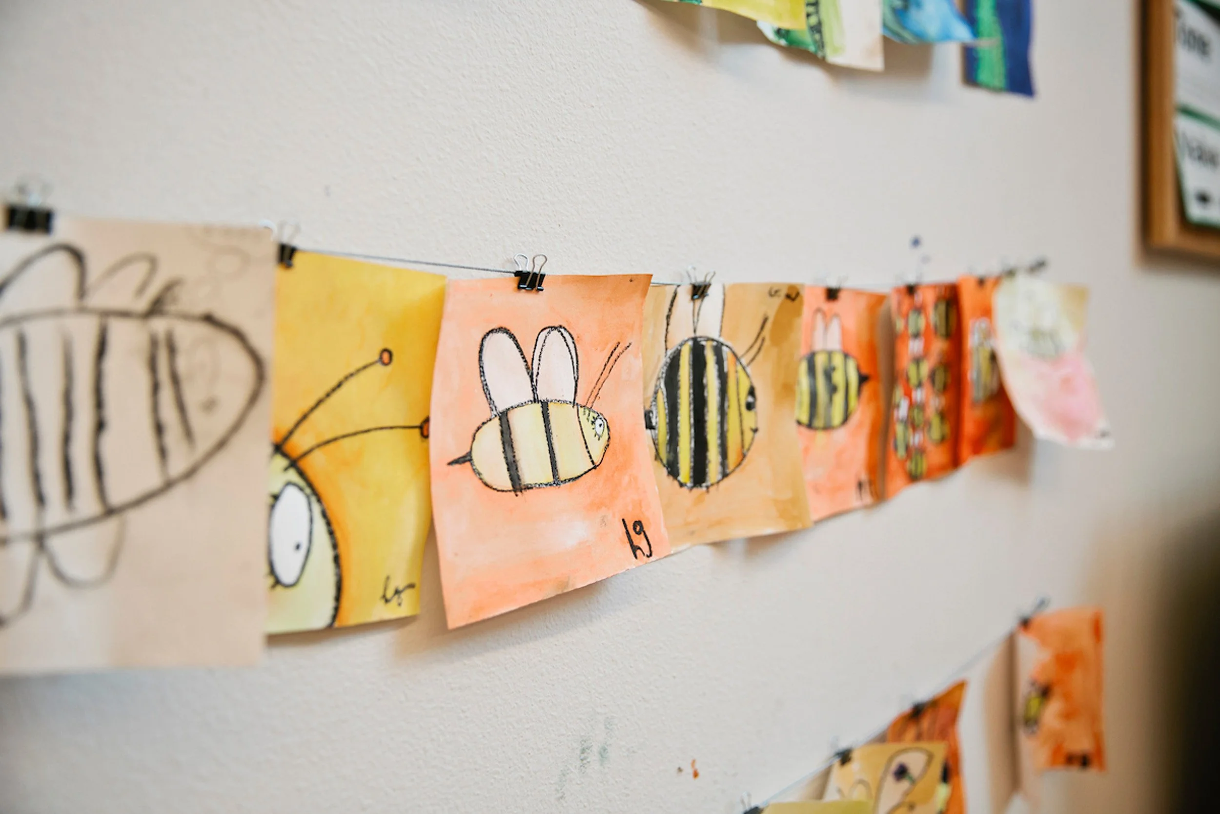 Children's artwork on string depicting bees with colorful backgrounds.
