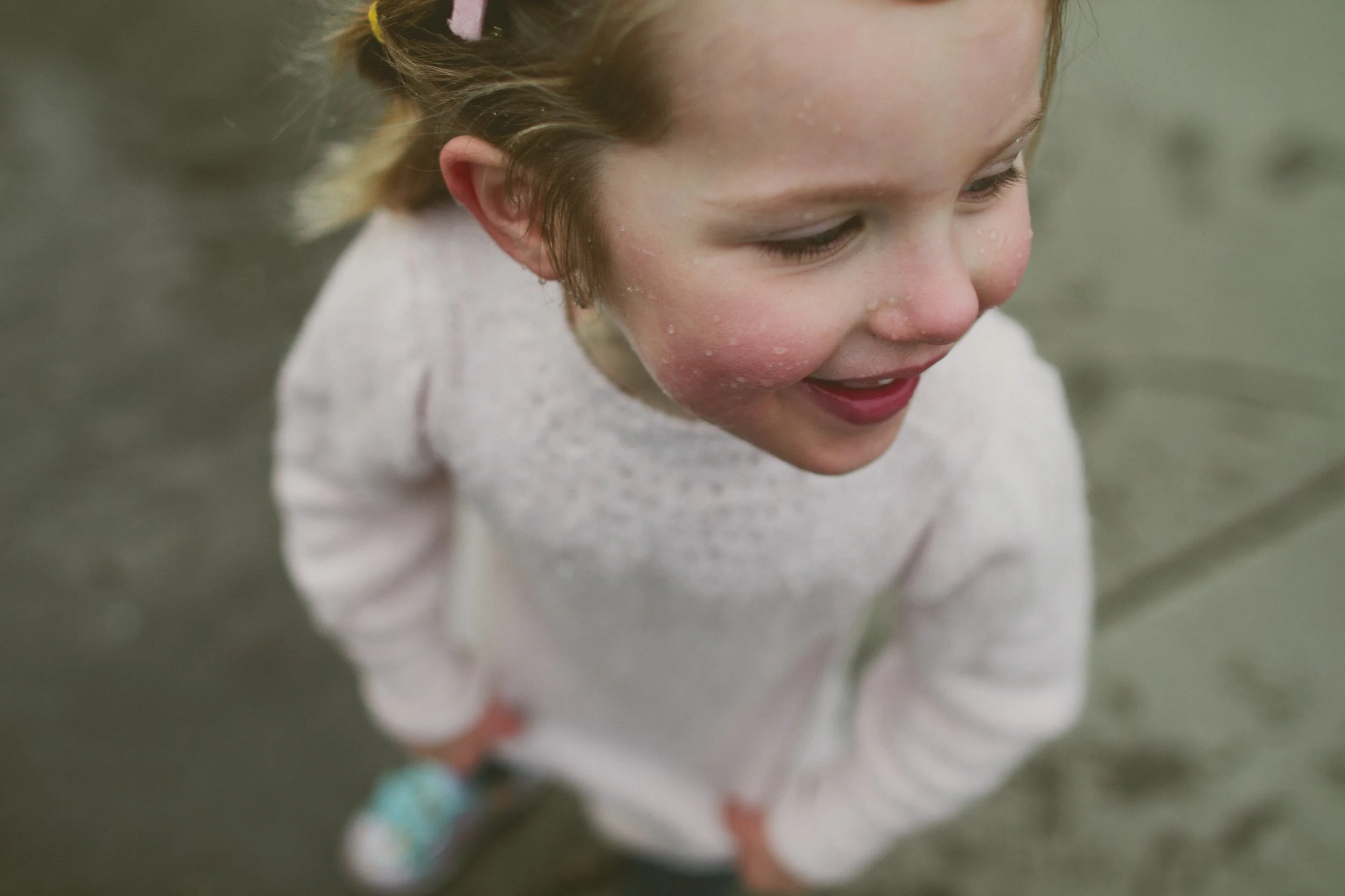 A young girl with wet hair and rosy cheeks smiling outdoors.