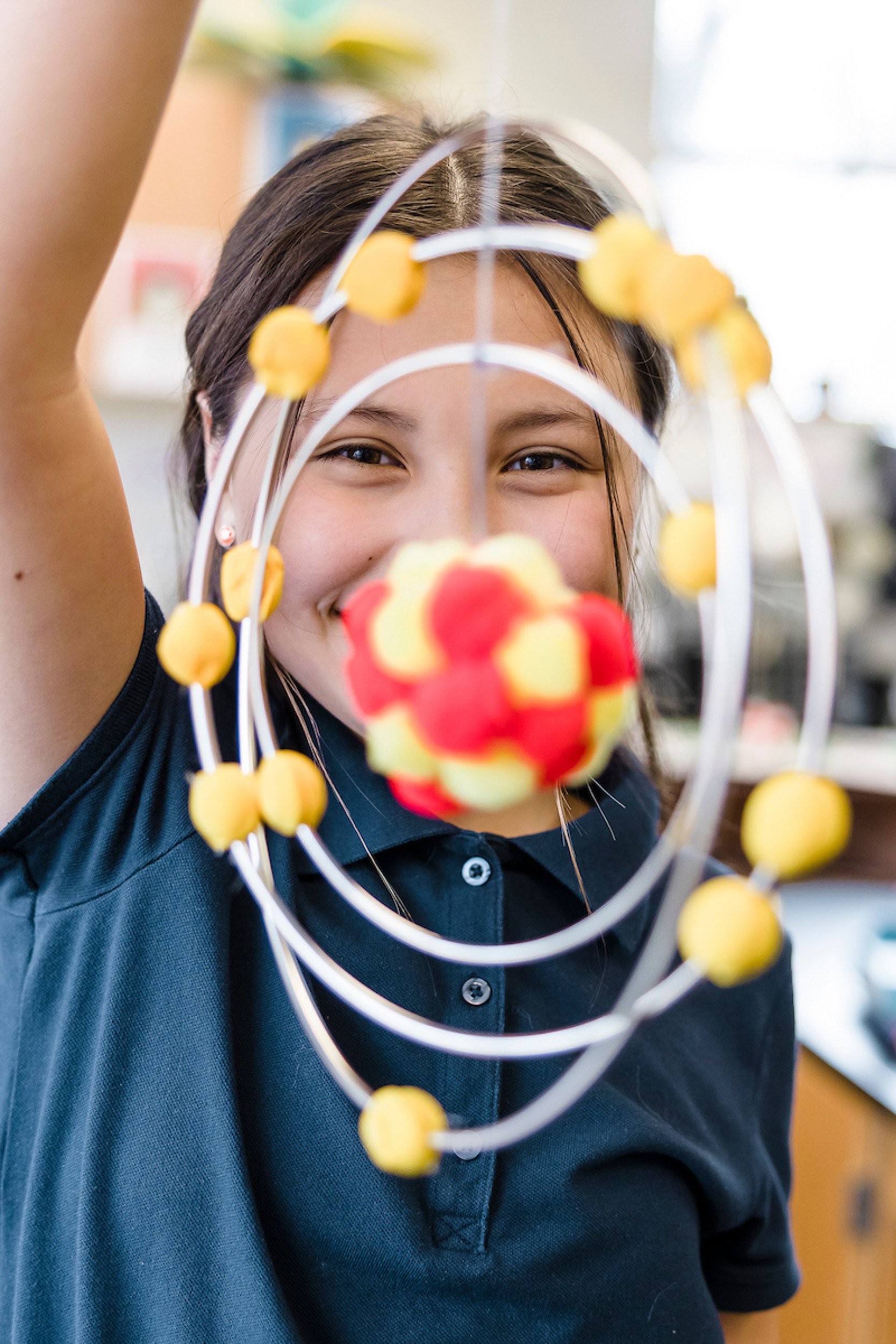 A girl smiling and holding a molecular model made of colored balls and wires.