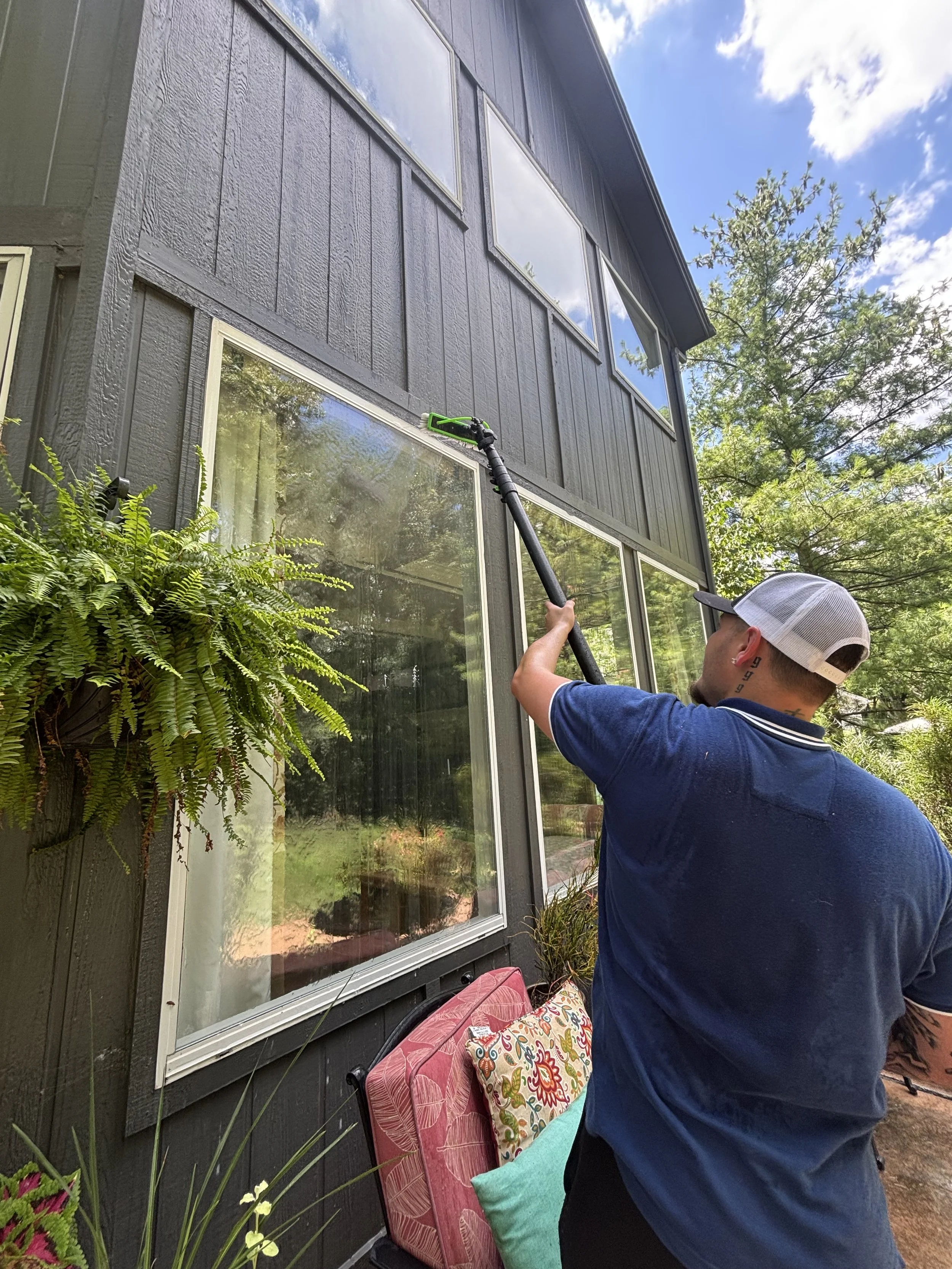 Person pressure washing the exterior of a house's second-story porch.