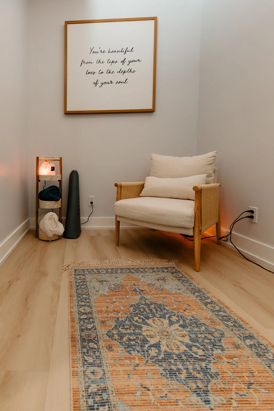 Salt lounge with chair, yoga mat, small 3 tiered cabinet with blankets and salt lamp on it