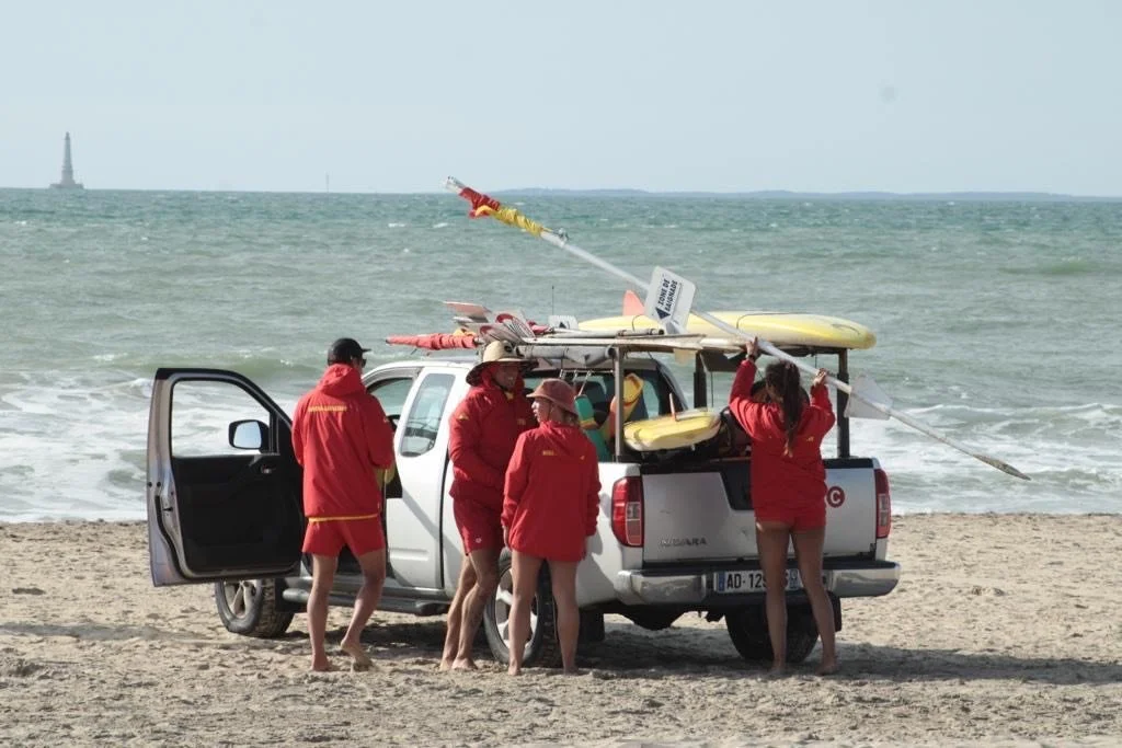 Group of people in red jackets preparing surfboards beside a pickup truck on a beach.
