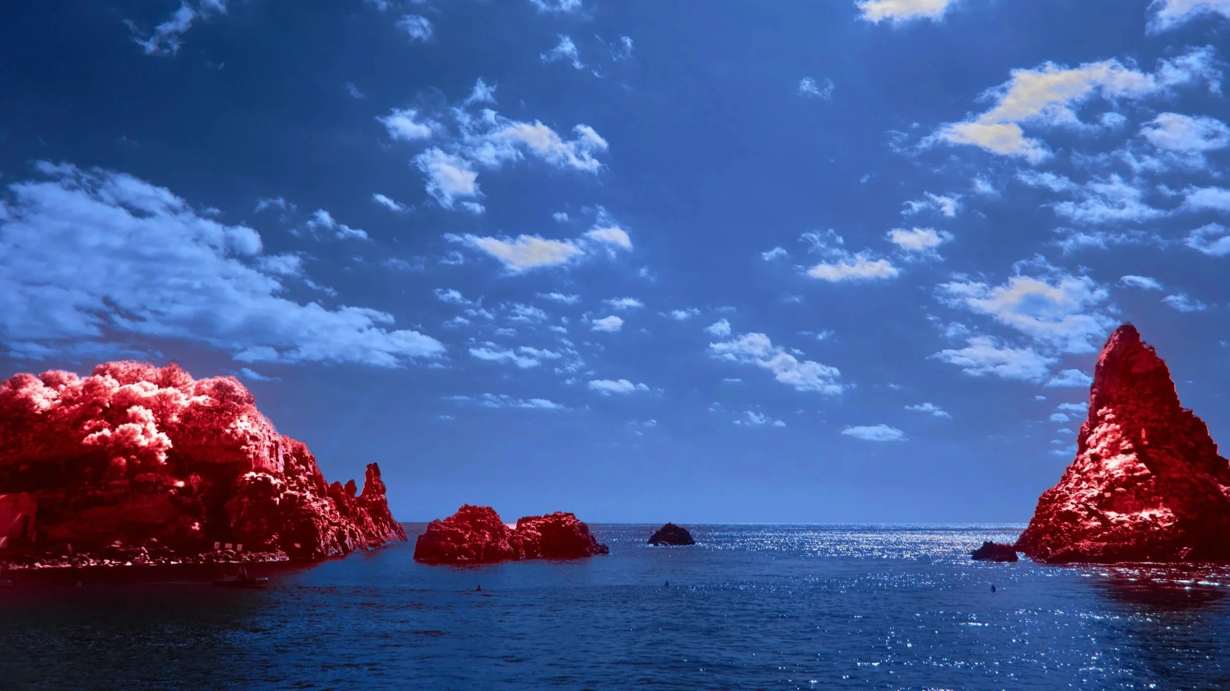 A coastal landscape with several rocky islands and cliffs in the ocean under a blue sky with scattered clouds.