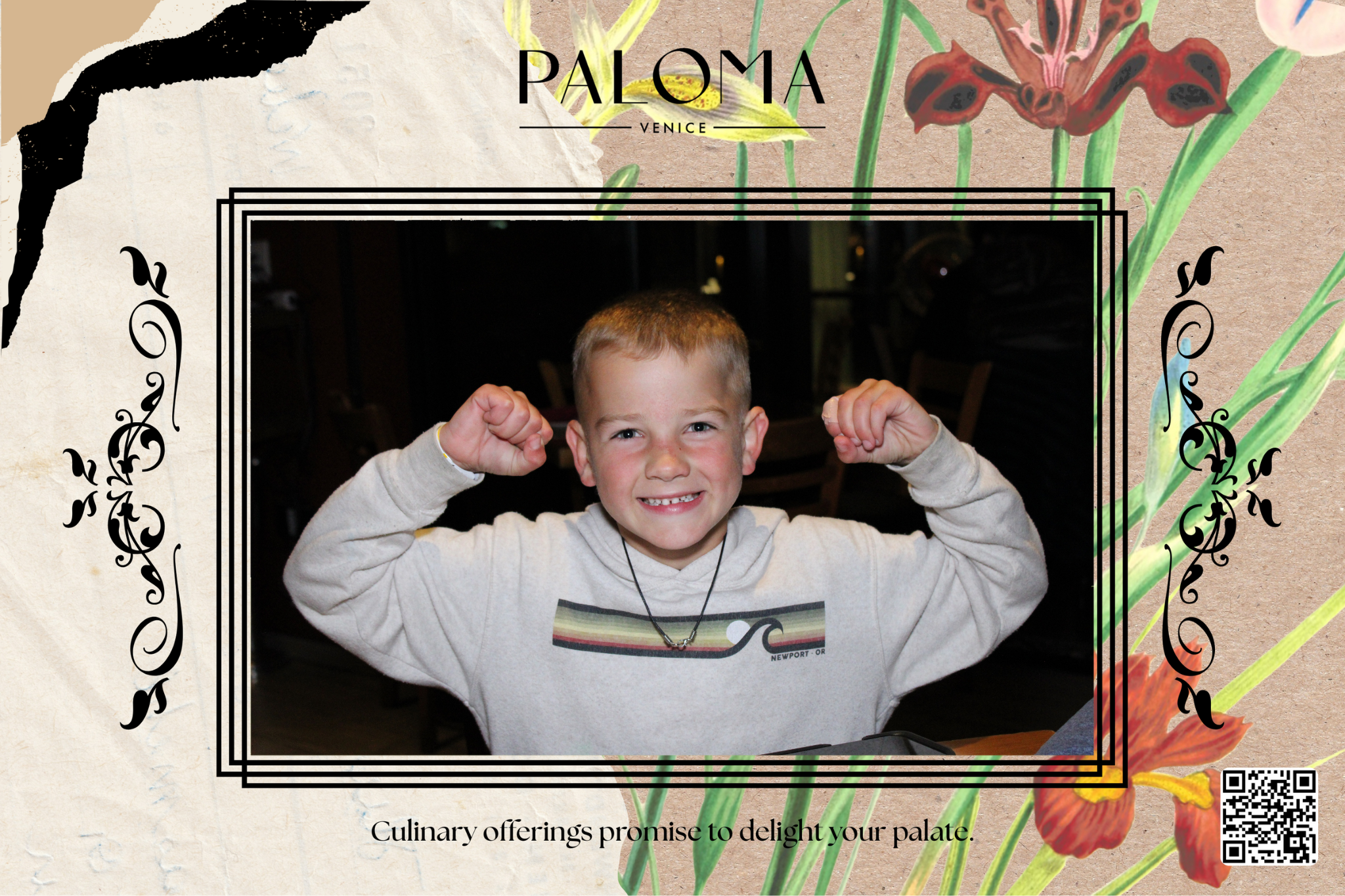 A young boy smiling and flexing his arms while sitting at a table inside a restaurant.