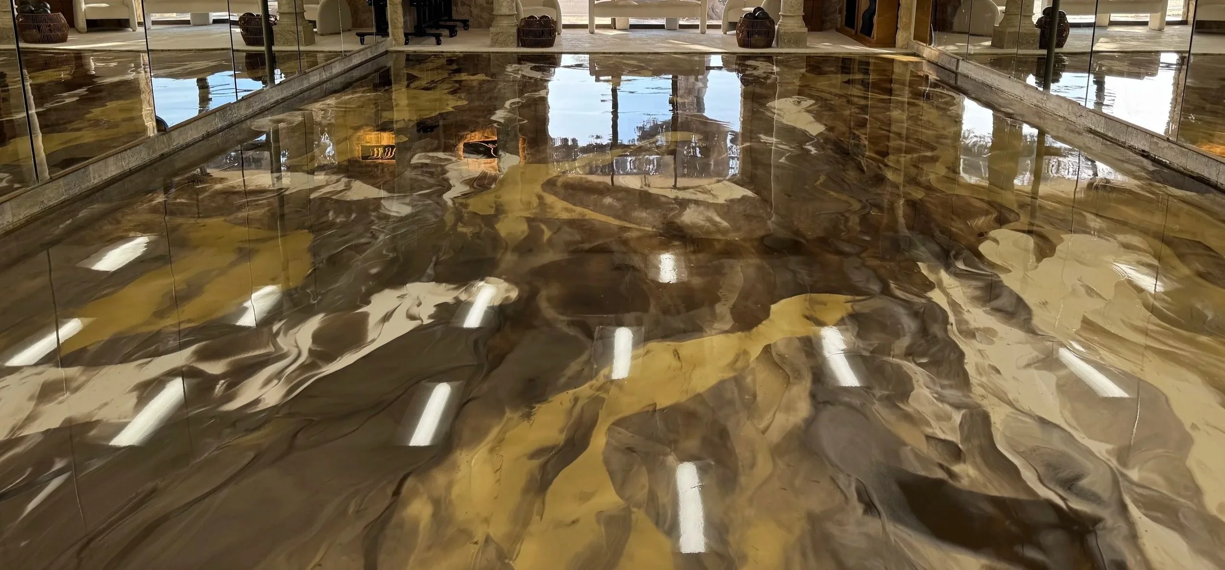 Stunning metallic epoxy showroom flooring featuring swirled brown, gold, and cream patterns creating dramatic 3D marble effect with mirror-like reflections in professional retail environment.