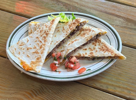 Plate of quesadillas with tomatoes and lettuce on wooden table in Brooklyn.