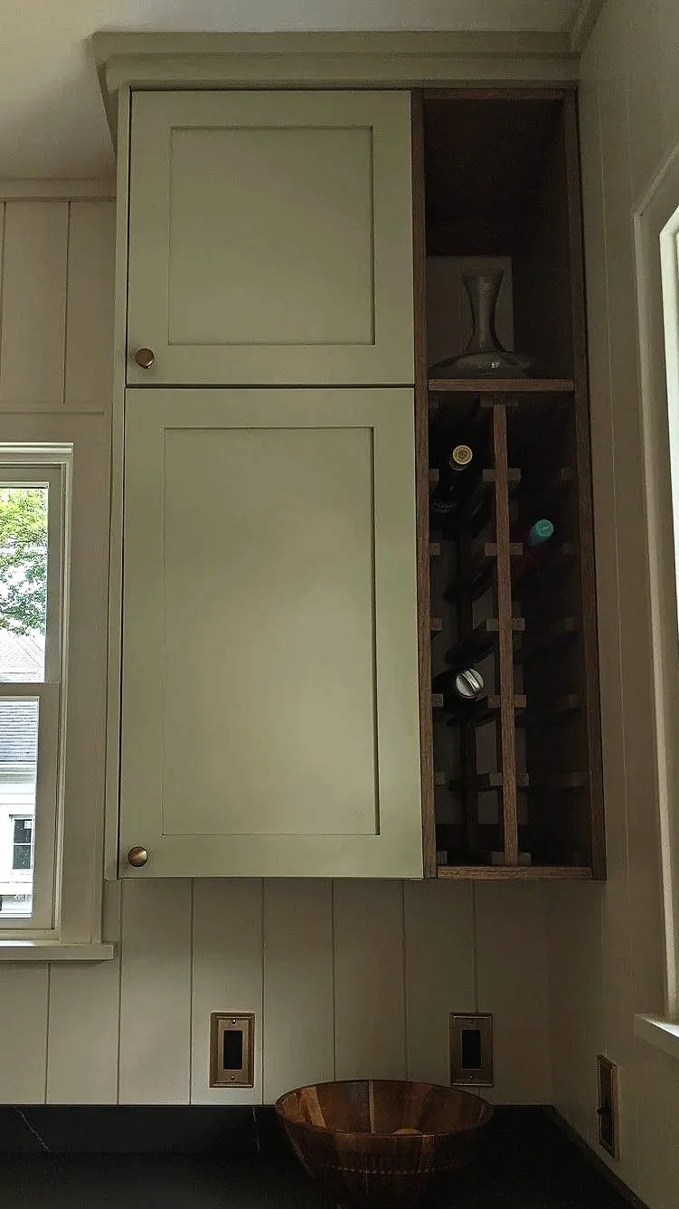 Kitchen cabinet with a frosted glass door on the left and an open wine rack on the right. The wine rack contains several bottles of wine and a glass decanter on top.