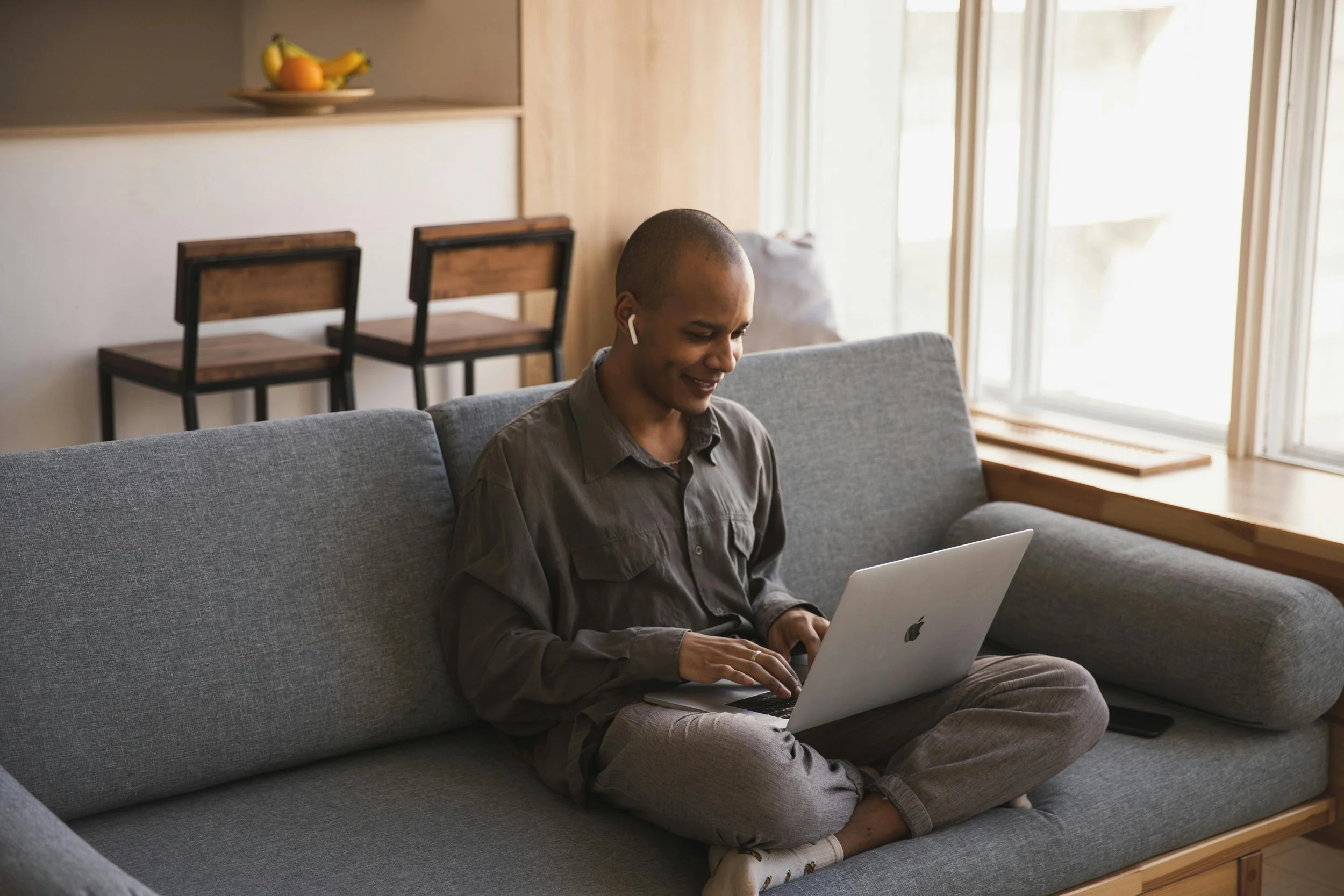 A young person sits on a gray shirt, looking at a laptop.