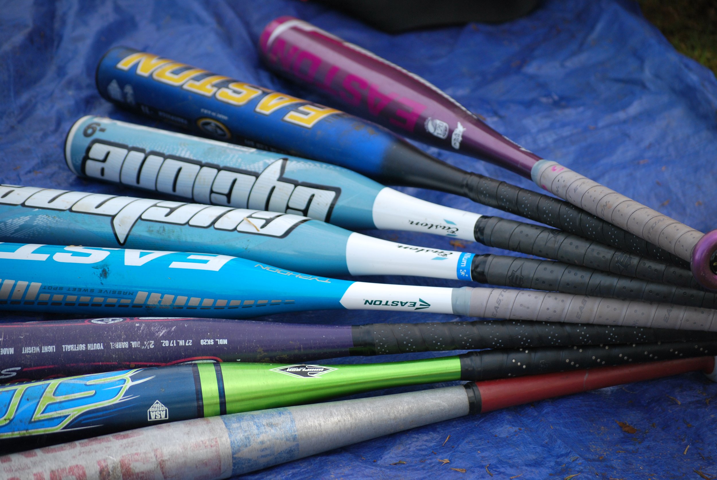 Several baseball bats with different colors and brands lying on a blue tarp.