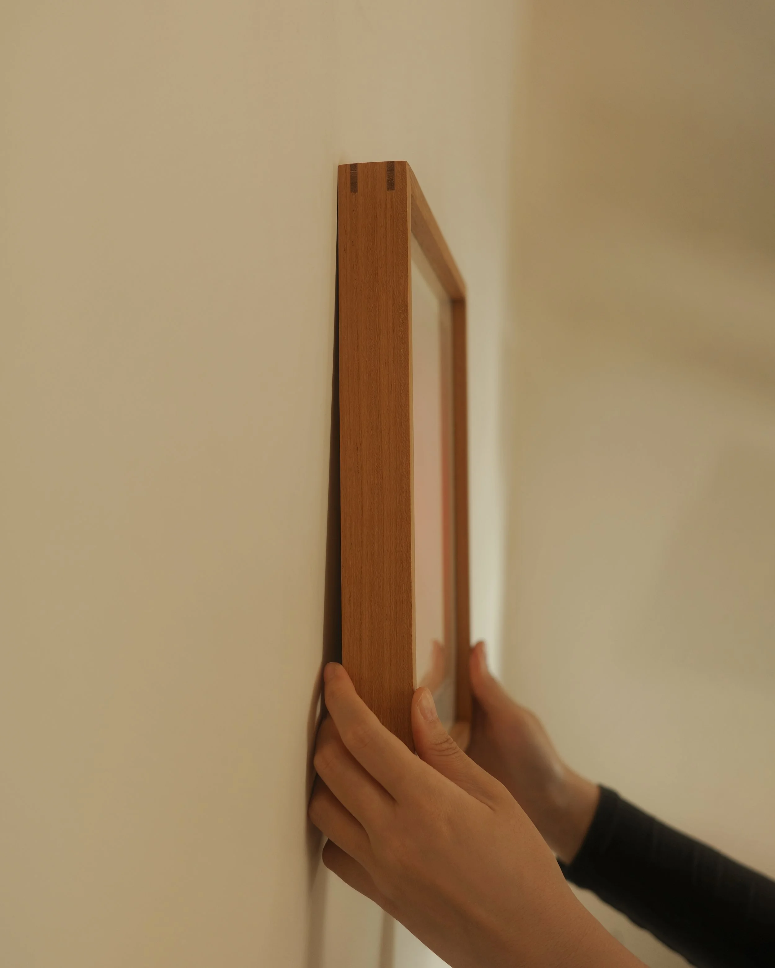 A person hanging a wooden COLOROF Art Print on a plain wall.