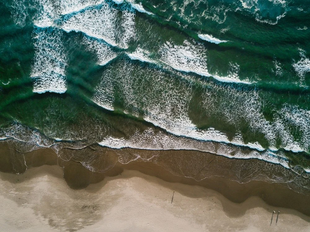 Overhead view of a sandy beach with green ocean waves crashing onto the shore.