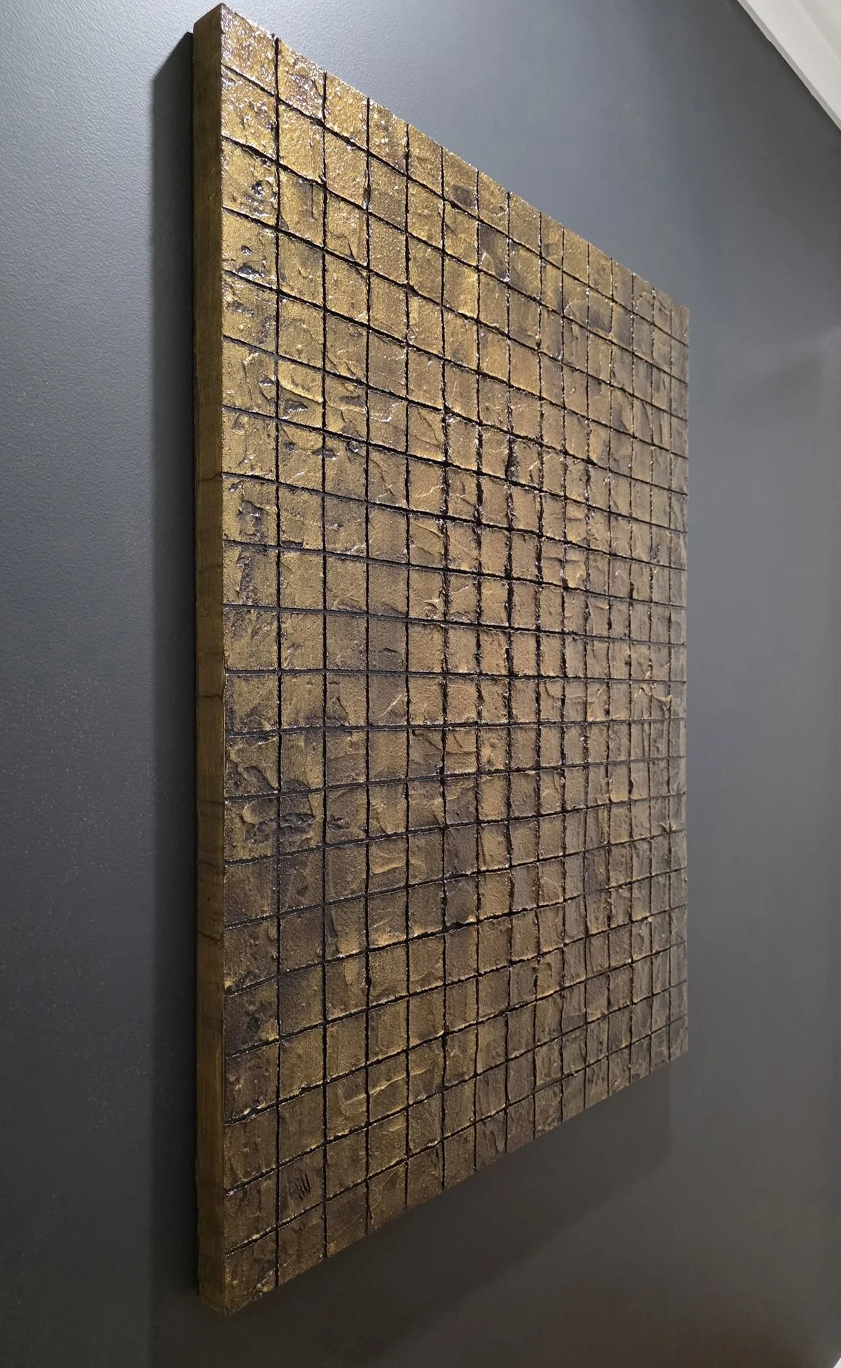 Side view of Obelisk VI : After mounted on a dark wall – highlights depth of cement layers and gold‑brown grid.