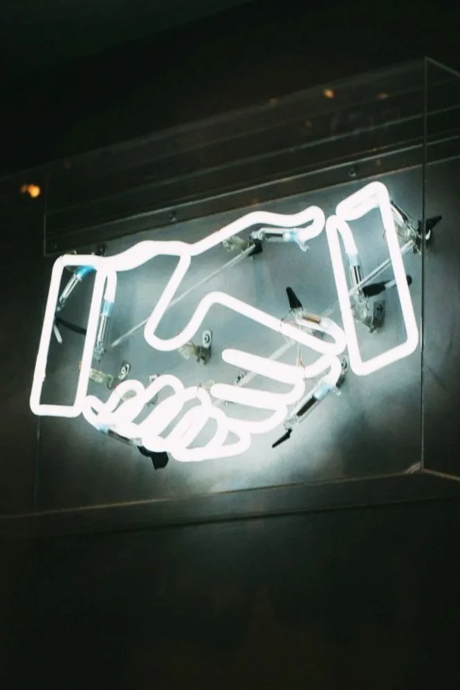 Neon sign of two hands shaking, symbolizing agreement or partnership.