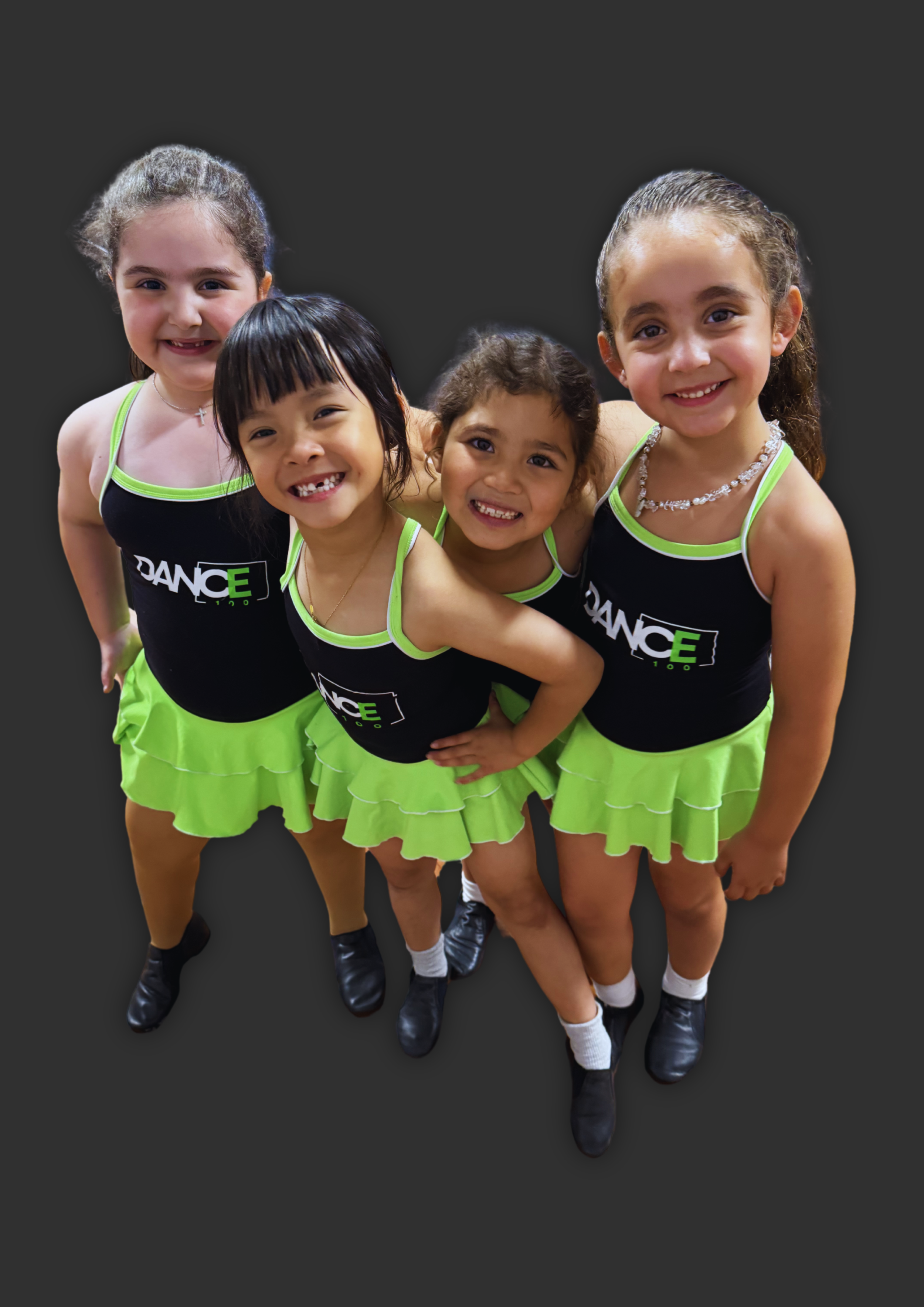Four young girls in black and green dance uniforms smiling and posing together.