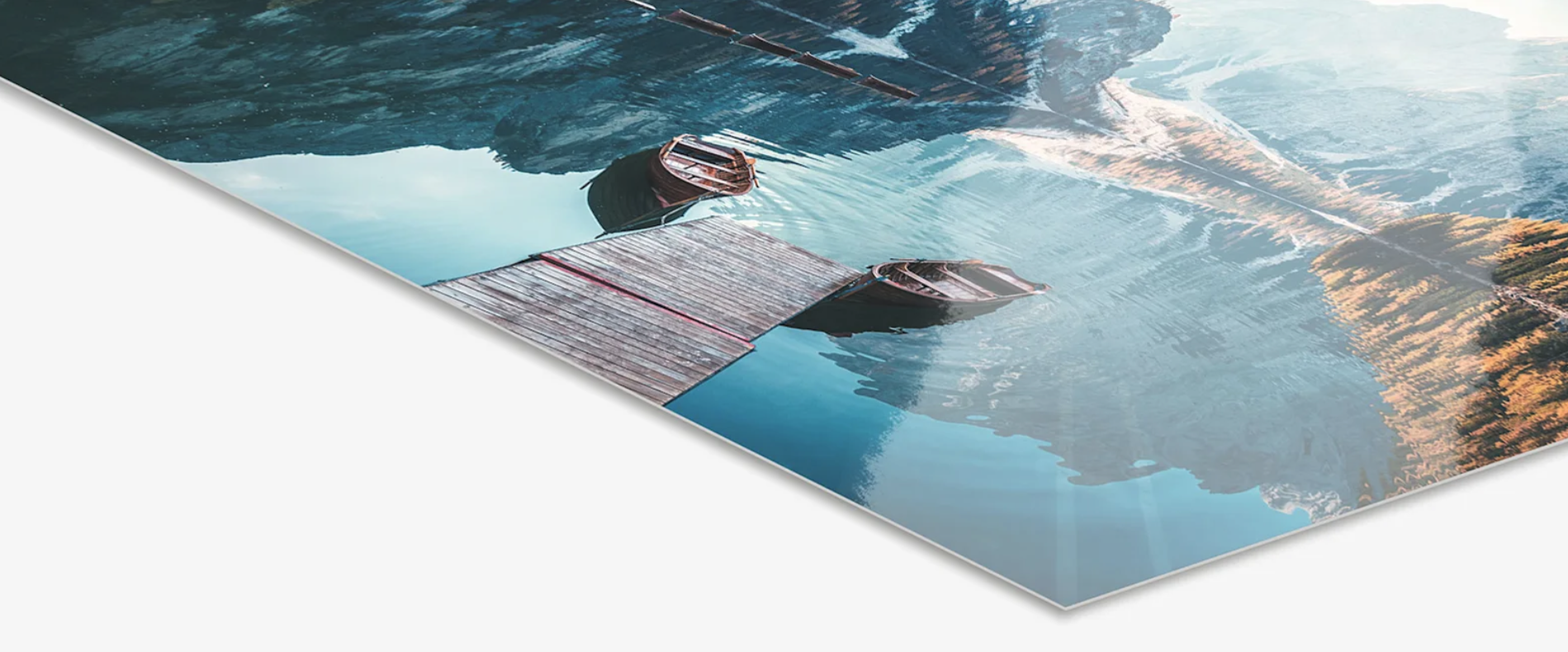 Reflected image of a mountain landscape with trees and a cloudy sky on a glossy poster or print, with a visible wooden dock and small boats at the bottom edge.