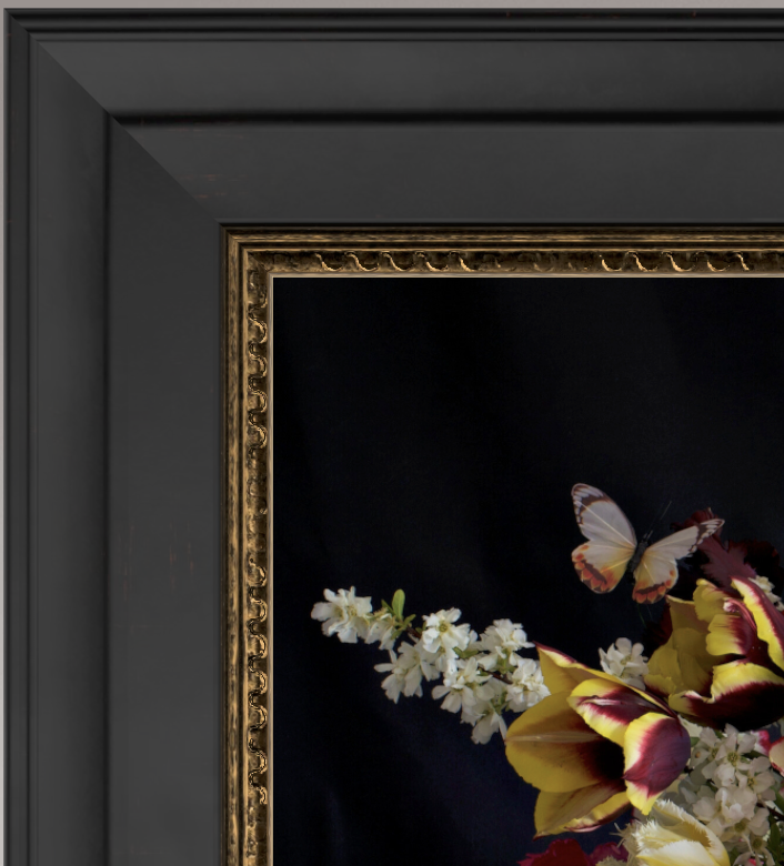 Close-up of a black and gold picture frame with a floral arrangement and a butterfly inside.
