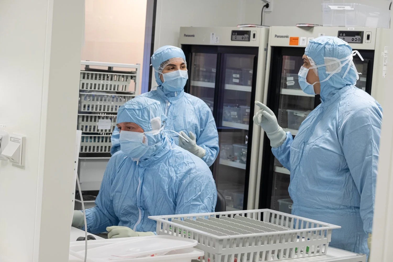 Ett medicinskt team av kollegor på Medovia i skyddsutrustning arbetar i ett laboratorium eller på sjukhus, med utrustning och kylskåp i bakgrunden.