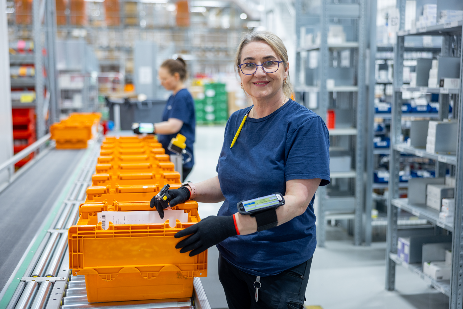 Kvinna på Medovia står i driften med orangea plastbackar och packar leveranser.