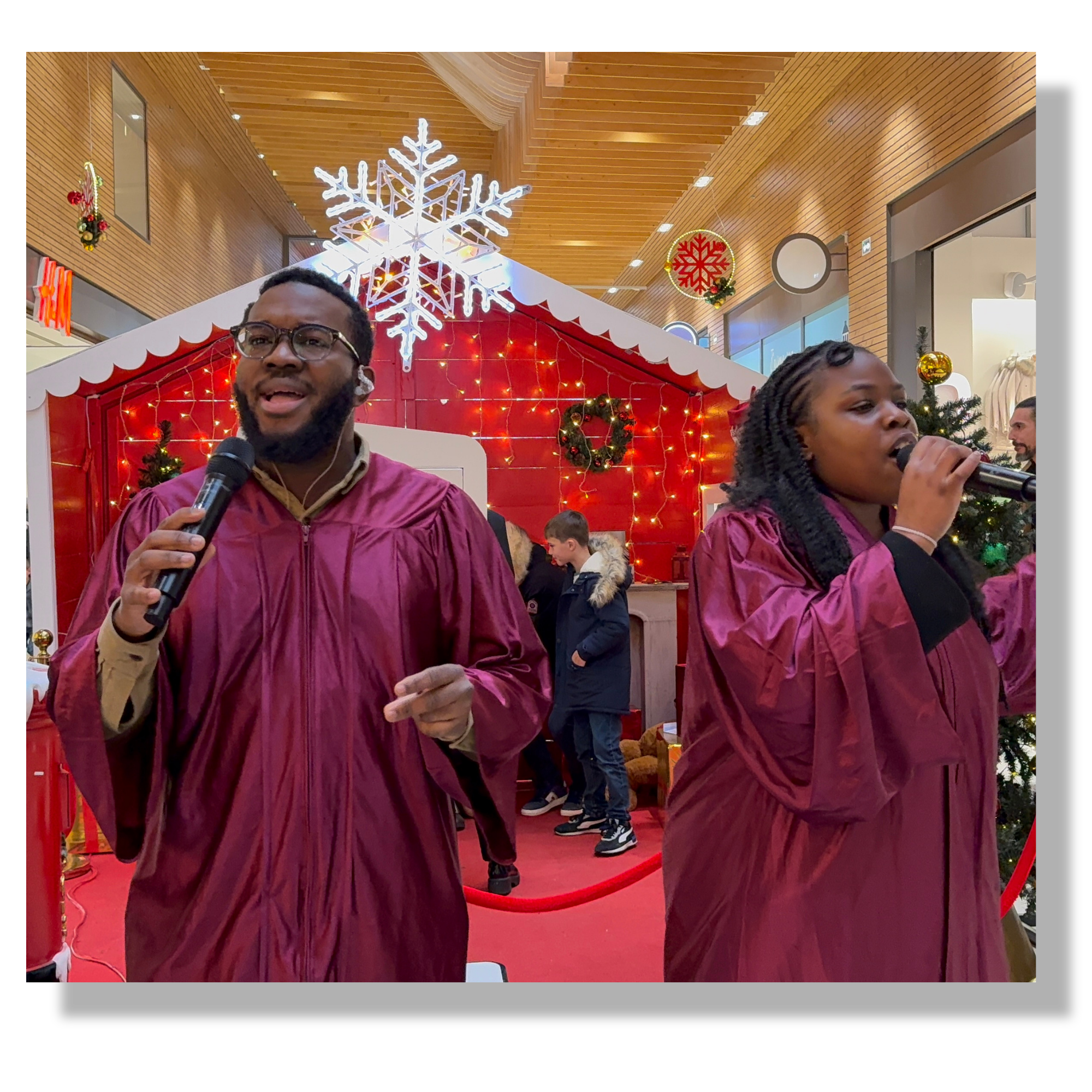 Deux personnes chantent avec des microphones dans une décoration de Noël dans un centre commercial en toges gospel pour une animation.