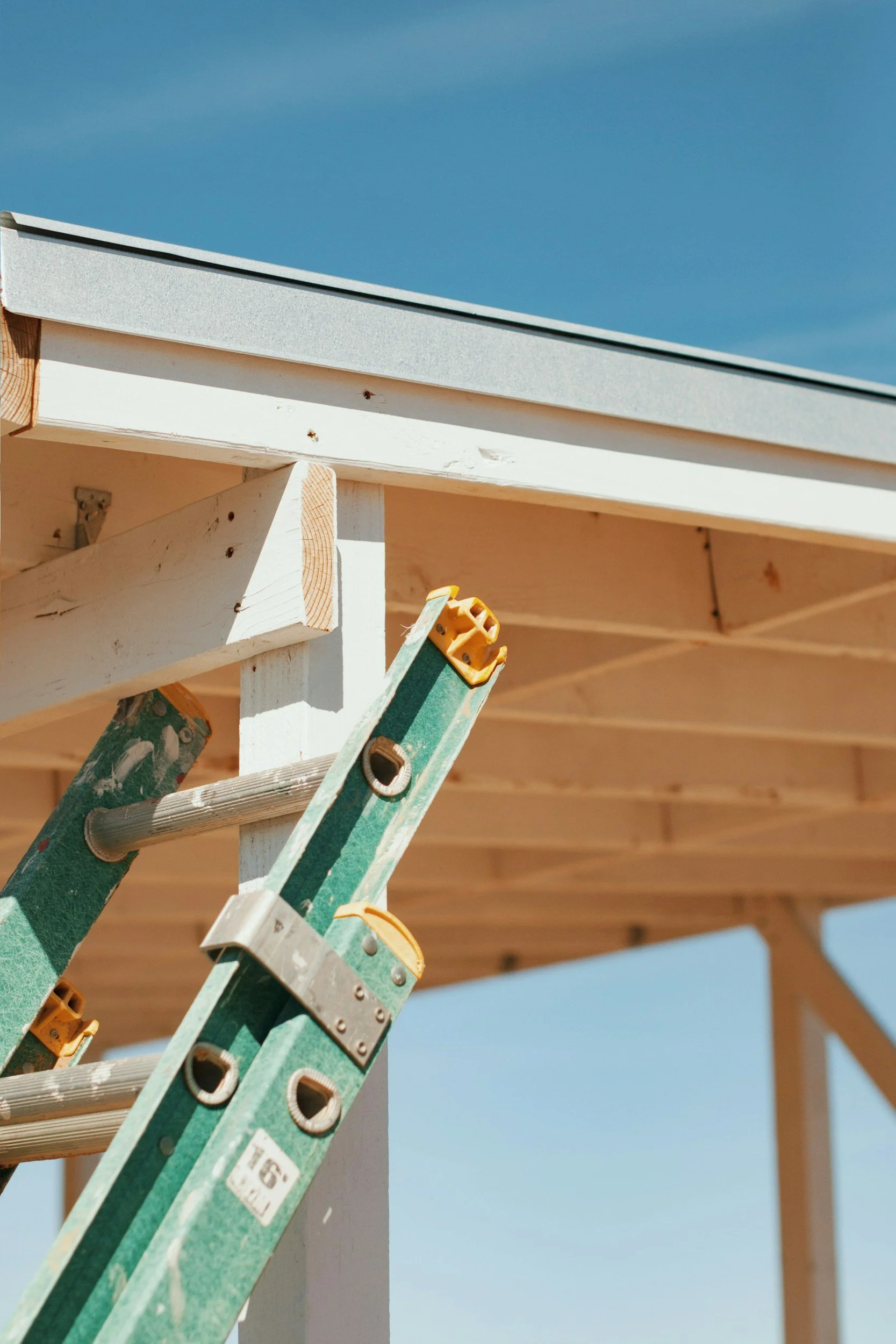 Construction ladder leaning against a partially built wooden structure with a blue sky background.