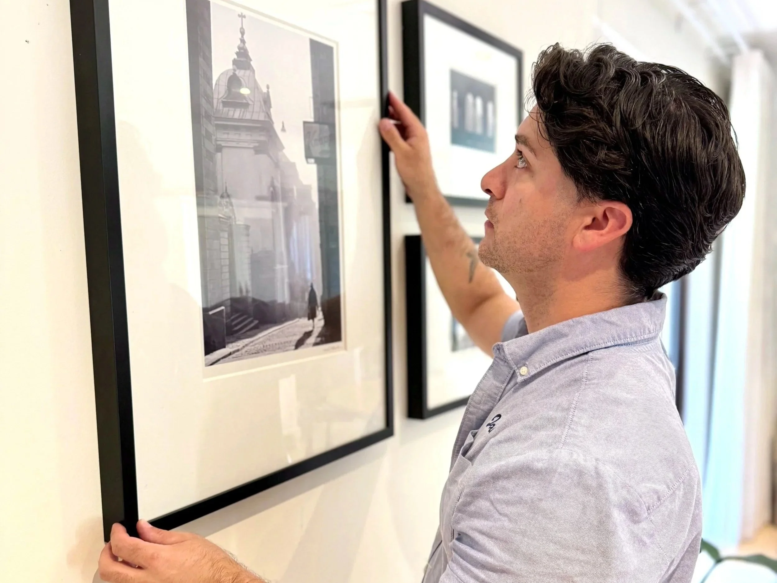 Jake's Maintenance hanging art frames on a gallery wall, looking at one of the framed pictures.