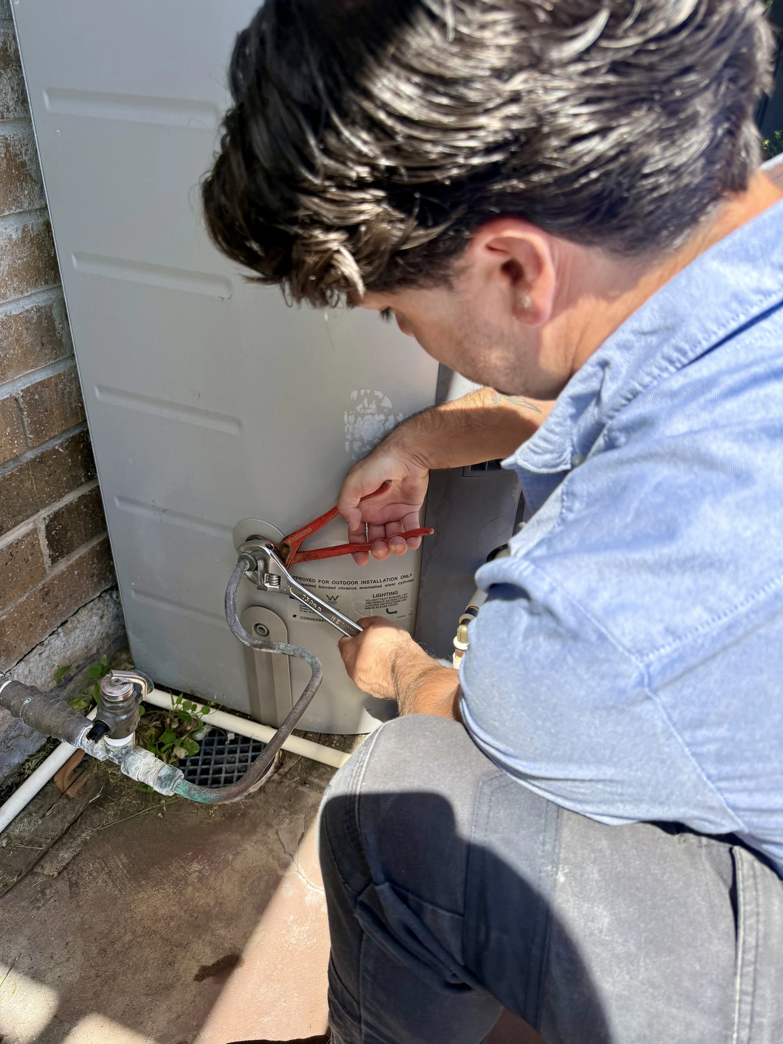 Plumber repairing hot water unit in Adelaide home